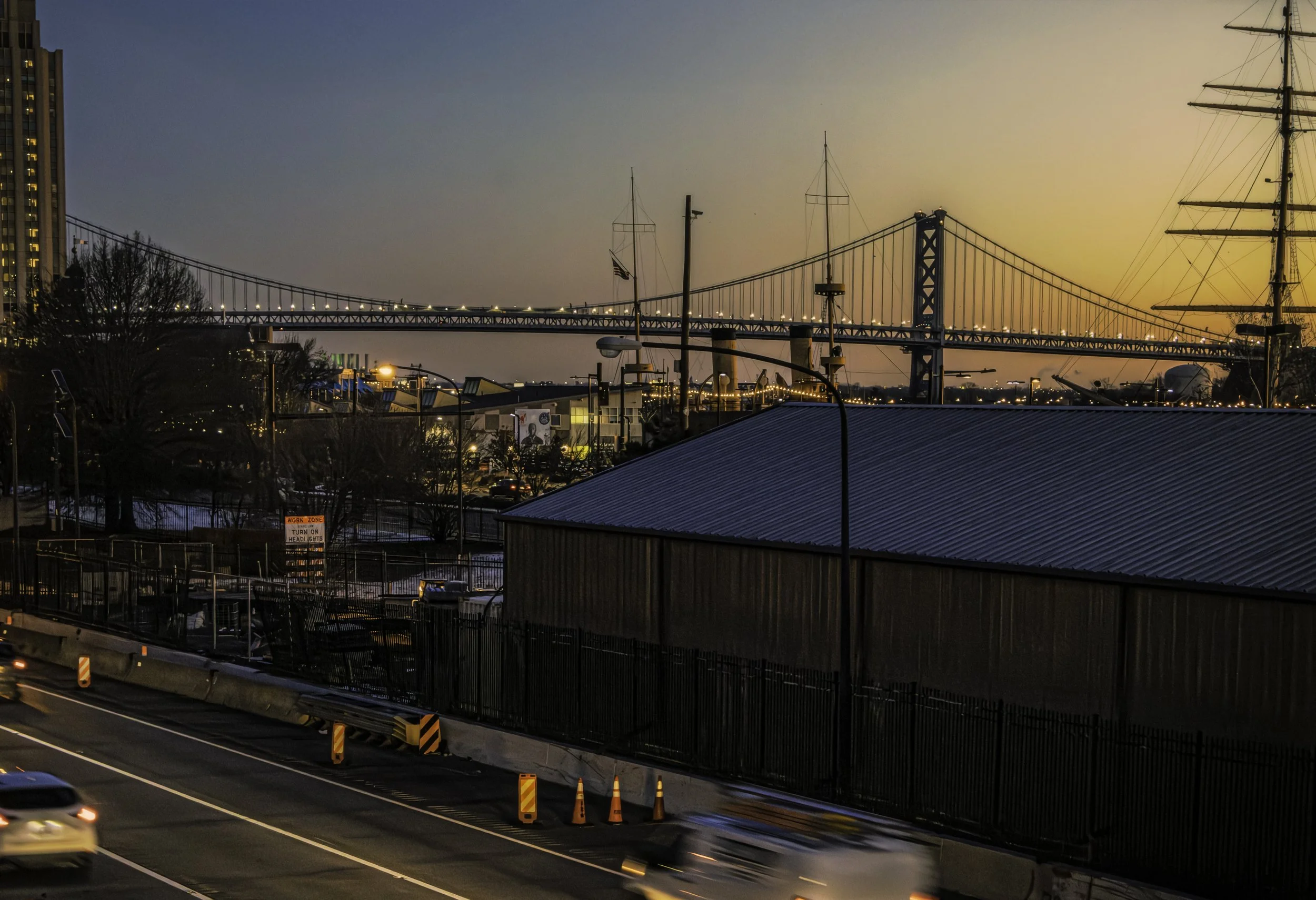 Rigging and First Light
Benjamin Franklin Bridge at dawn above waterfront buildings and a roadway, with ship rigging visible at the right edge of the frame.