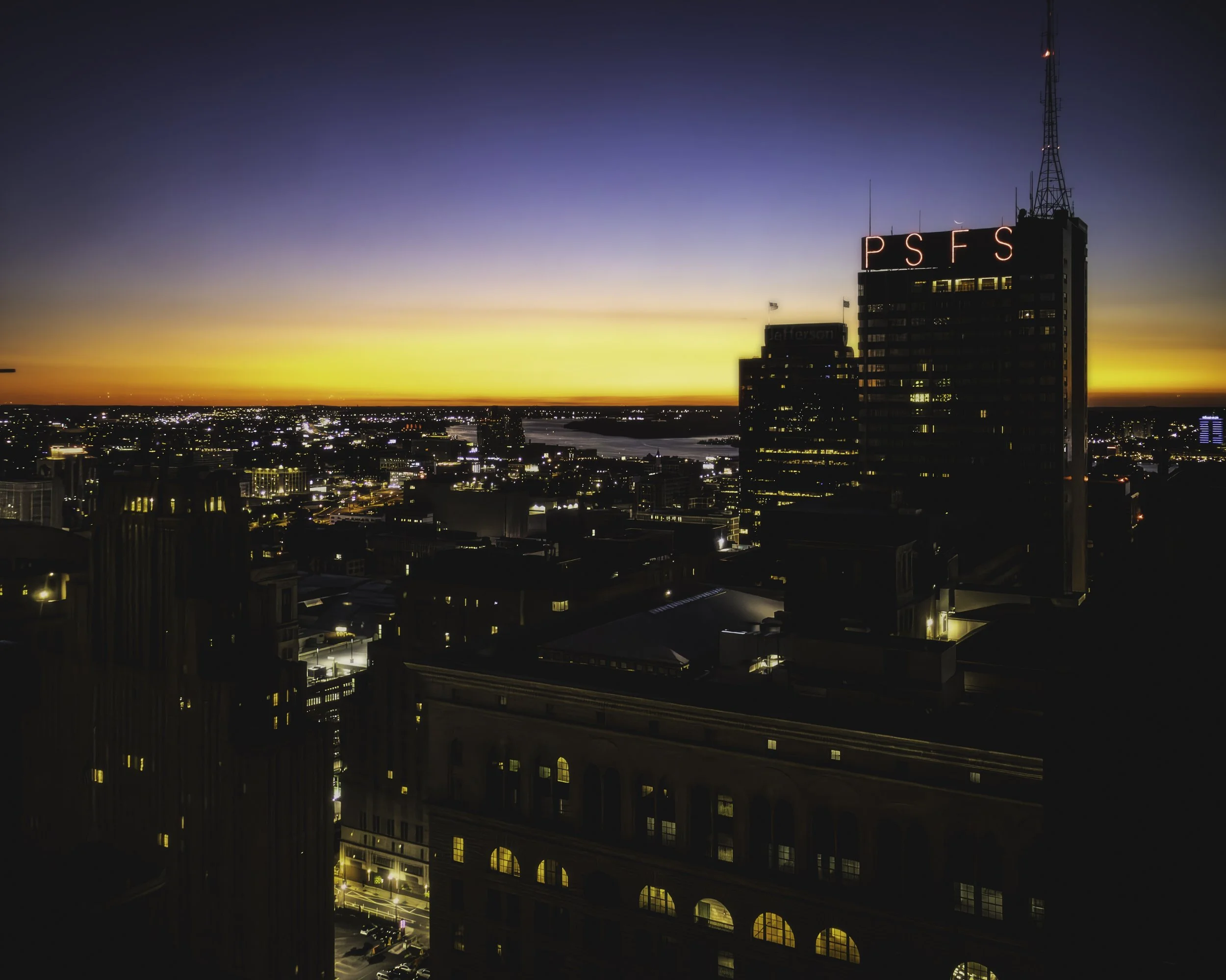 Morning Over Philadelphia
Philadelphia skyline at sunrise with the illuminated PSFS building rising above the city and warm light along the horizon.