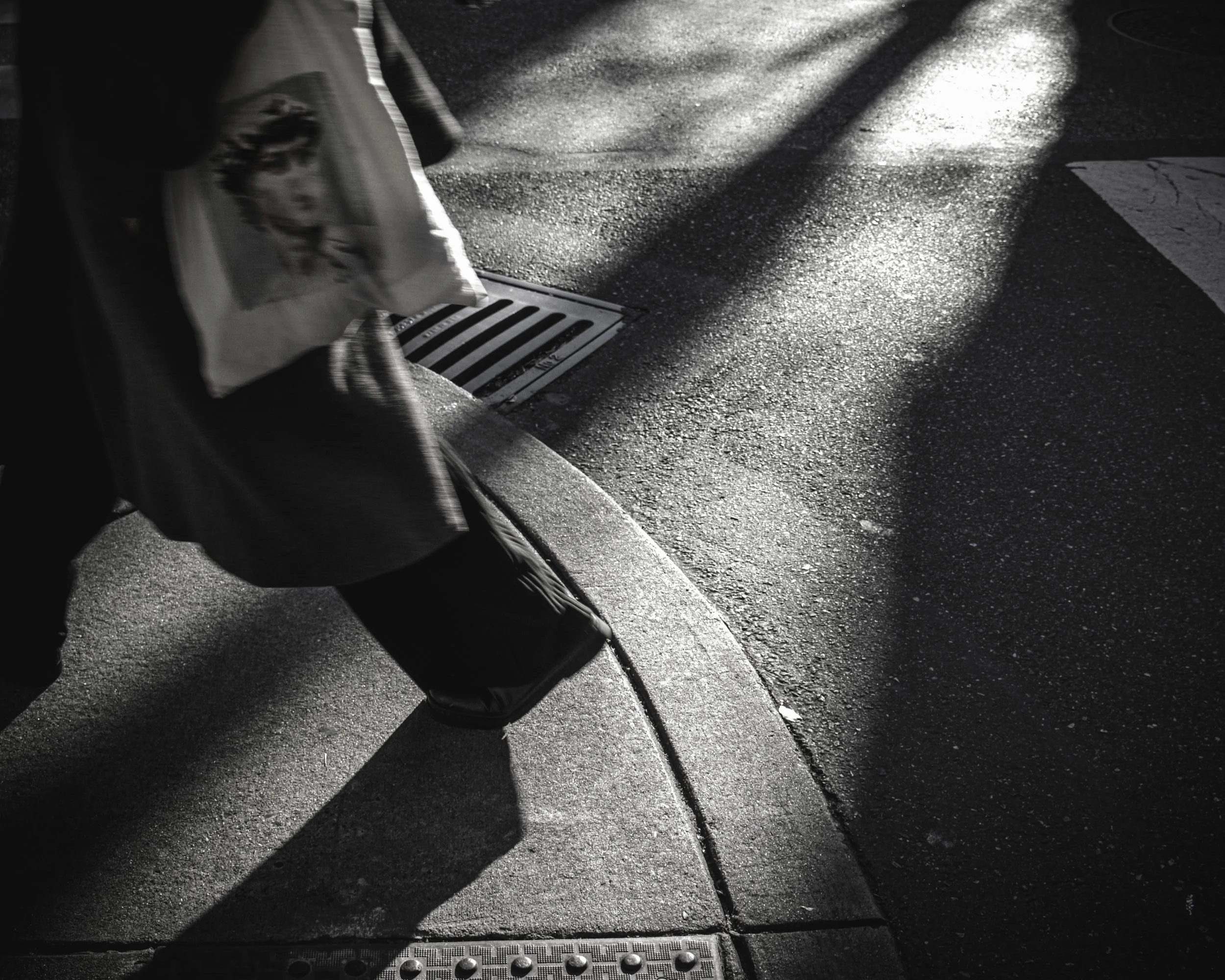 Bags and Long Shadows
Black and white close-up of a pedestrian stepping off a curb with shopping bags at 13th and Spruce Street, as long shadows stretch across wet pavement.