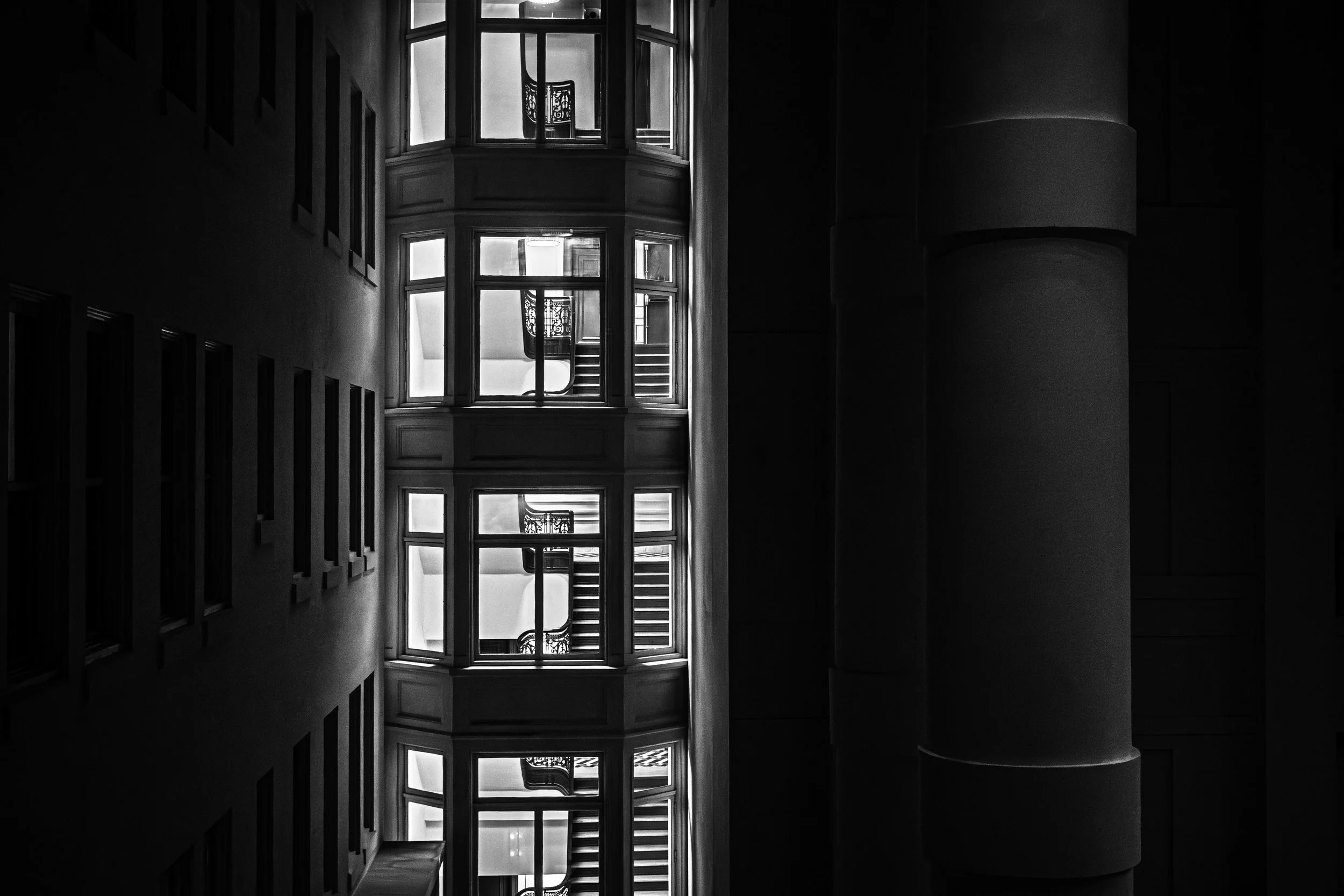 Bellevue Interior Study
Black and white architectural photograph of illuminated windows and staircases repeating through a narrow gap at The Bellevue.