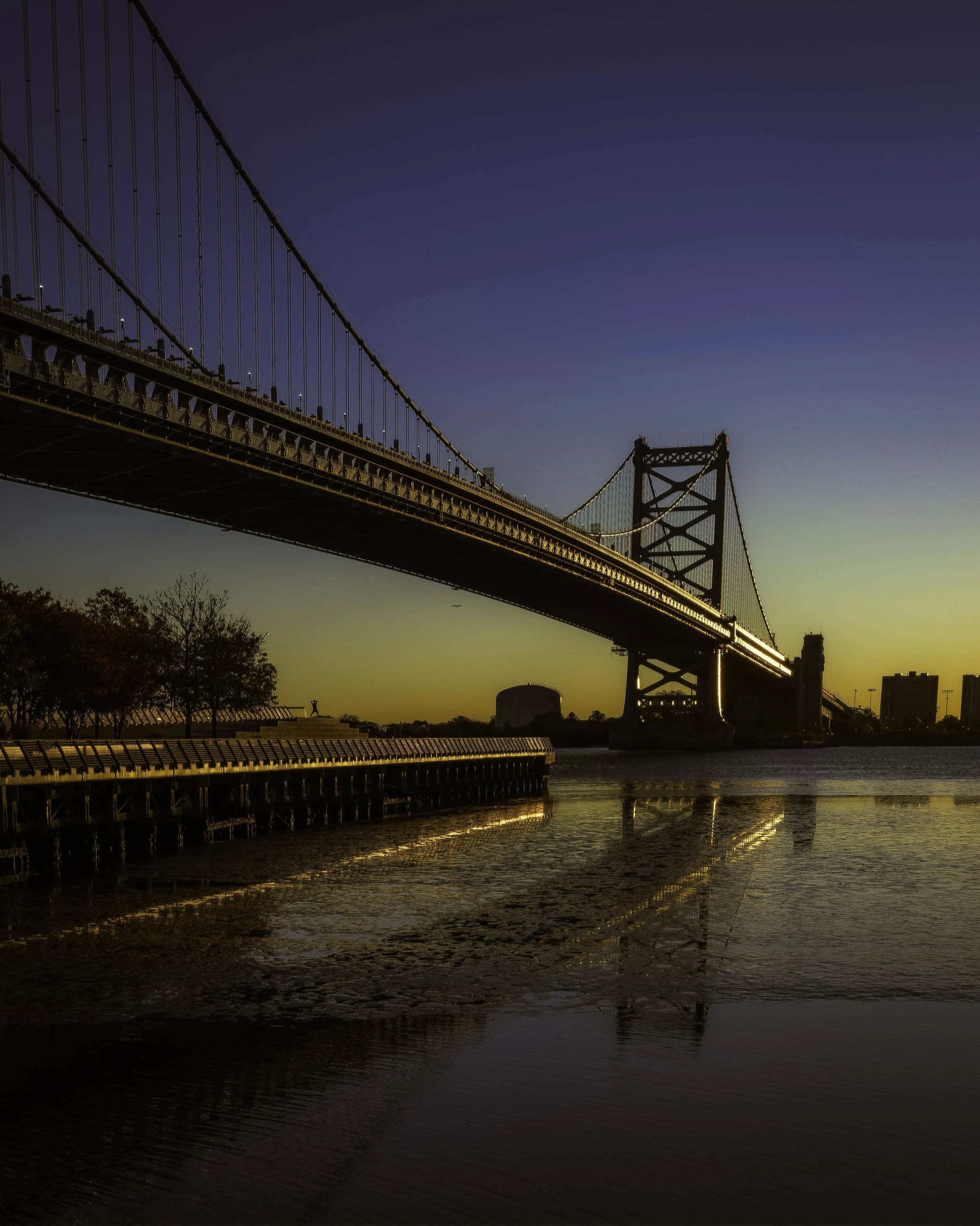 Contemplative Golden Dawn
Benjamin Franklin Bridge at golden dawn, reflected in still water beside a long riverside walkway.