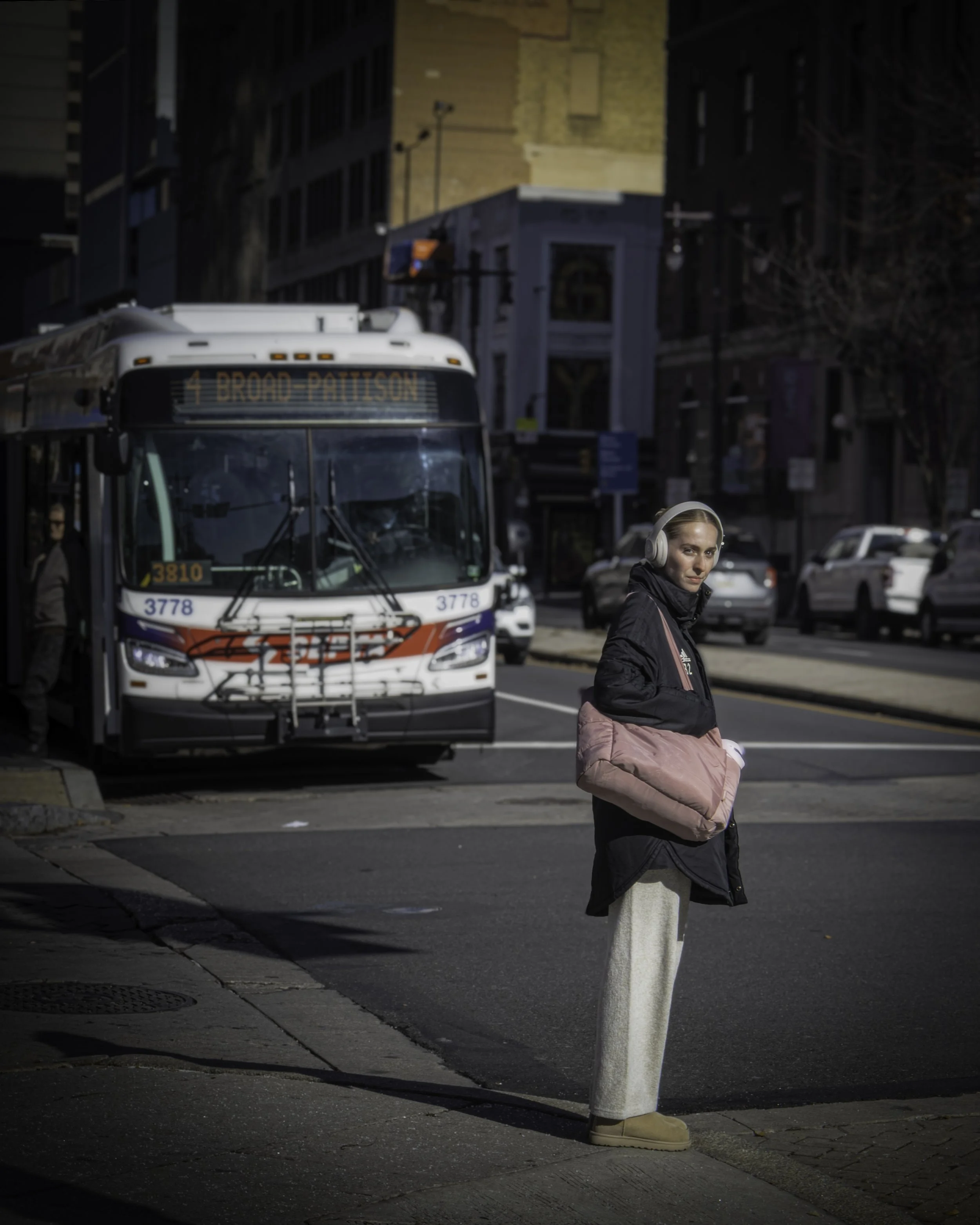 Waiting for the Right Moment
Woman wearing headphones waits at the curb with a city bus stopped behind her on a dim street.