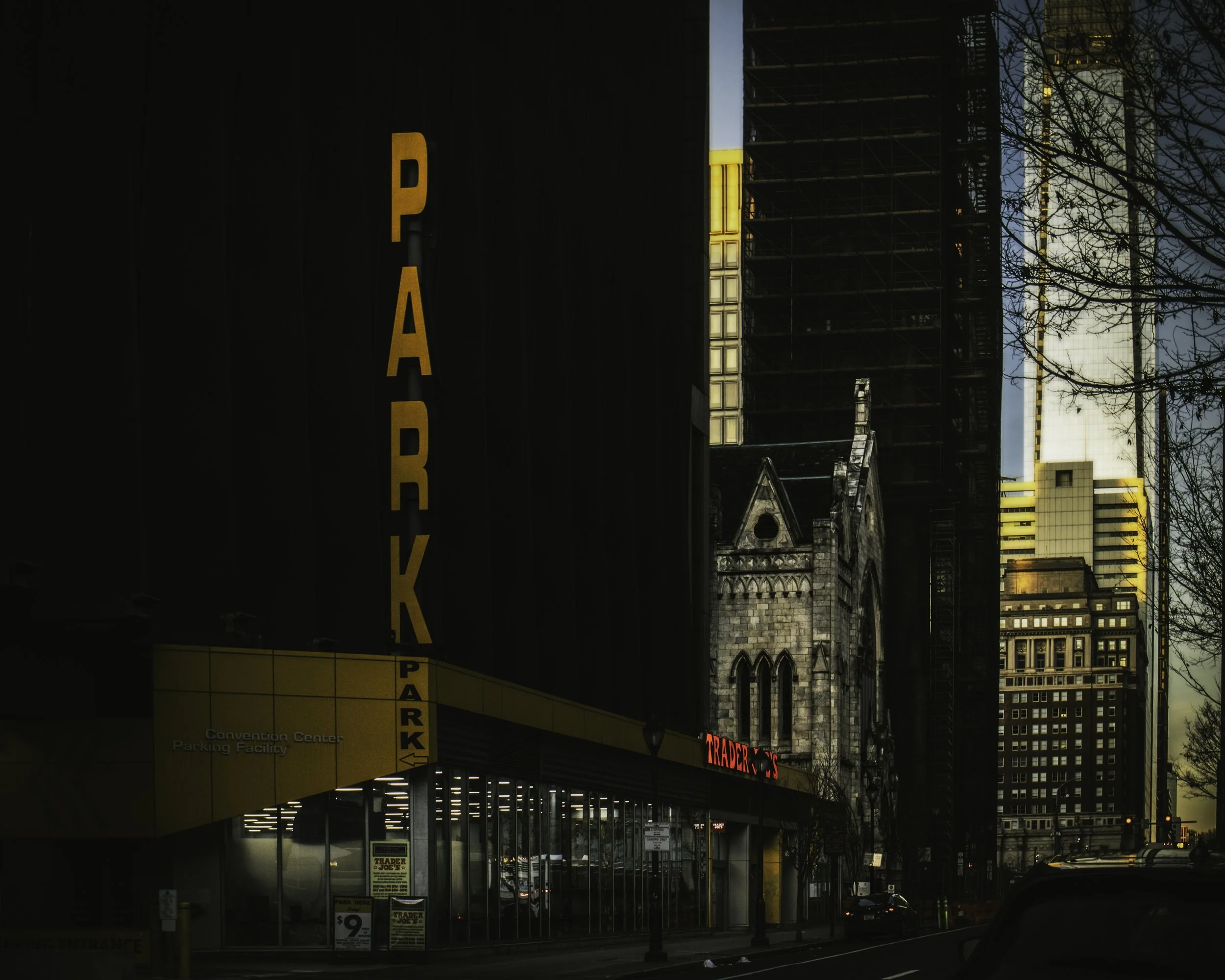 Towers Beyond the Garage
Downtown street view with a tall vertical PARK sign, dark building façades, and late light catching towers in the distance.