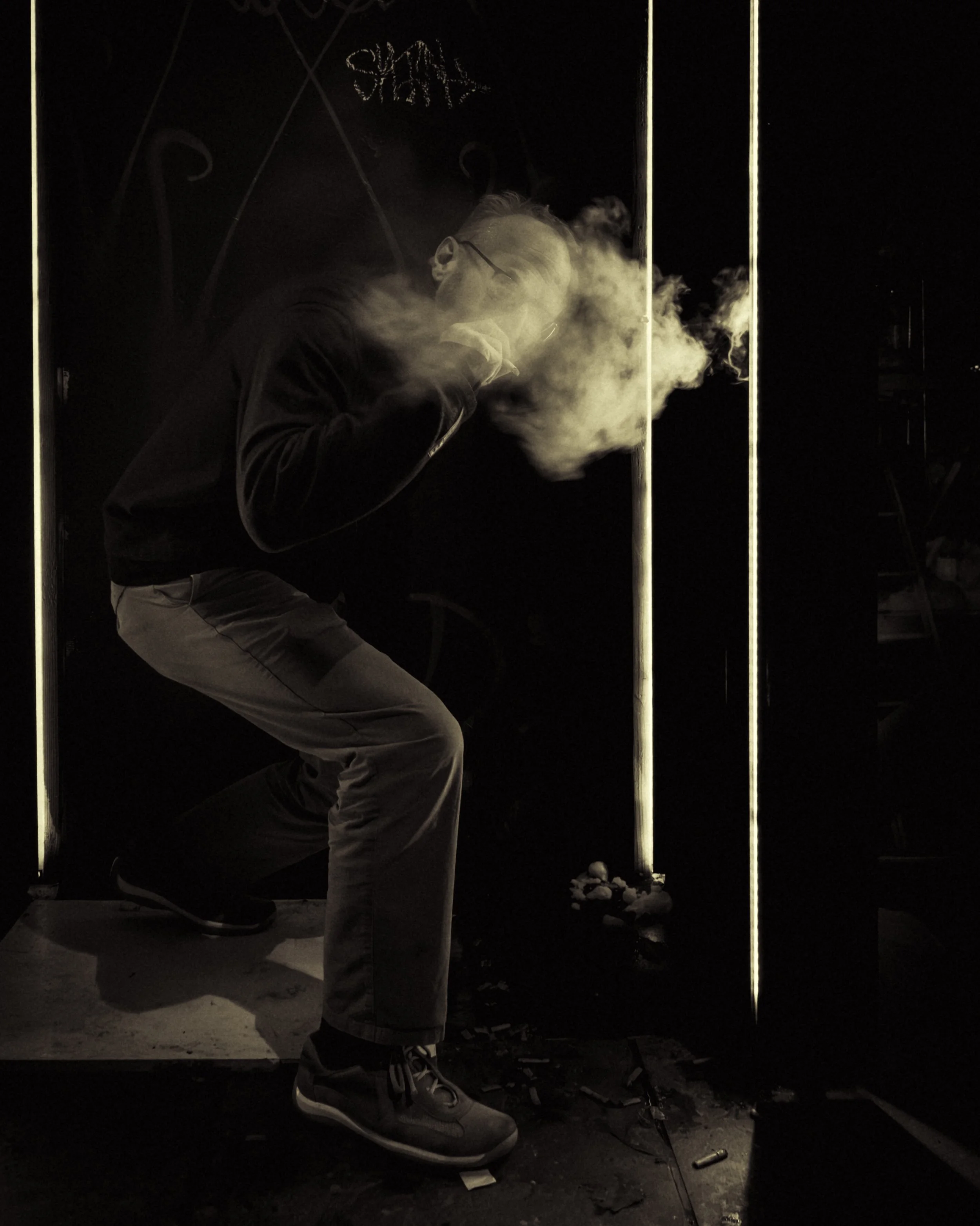 Between the Strips
Person crouches in a dark doorway as a cloud of vapor drifts across their face between narrow vertical strips of light.