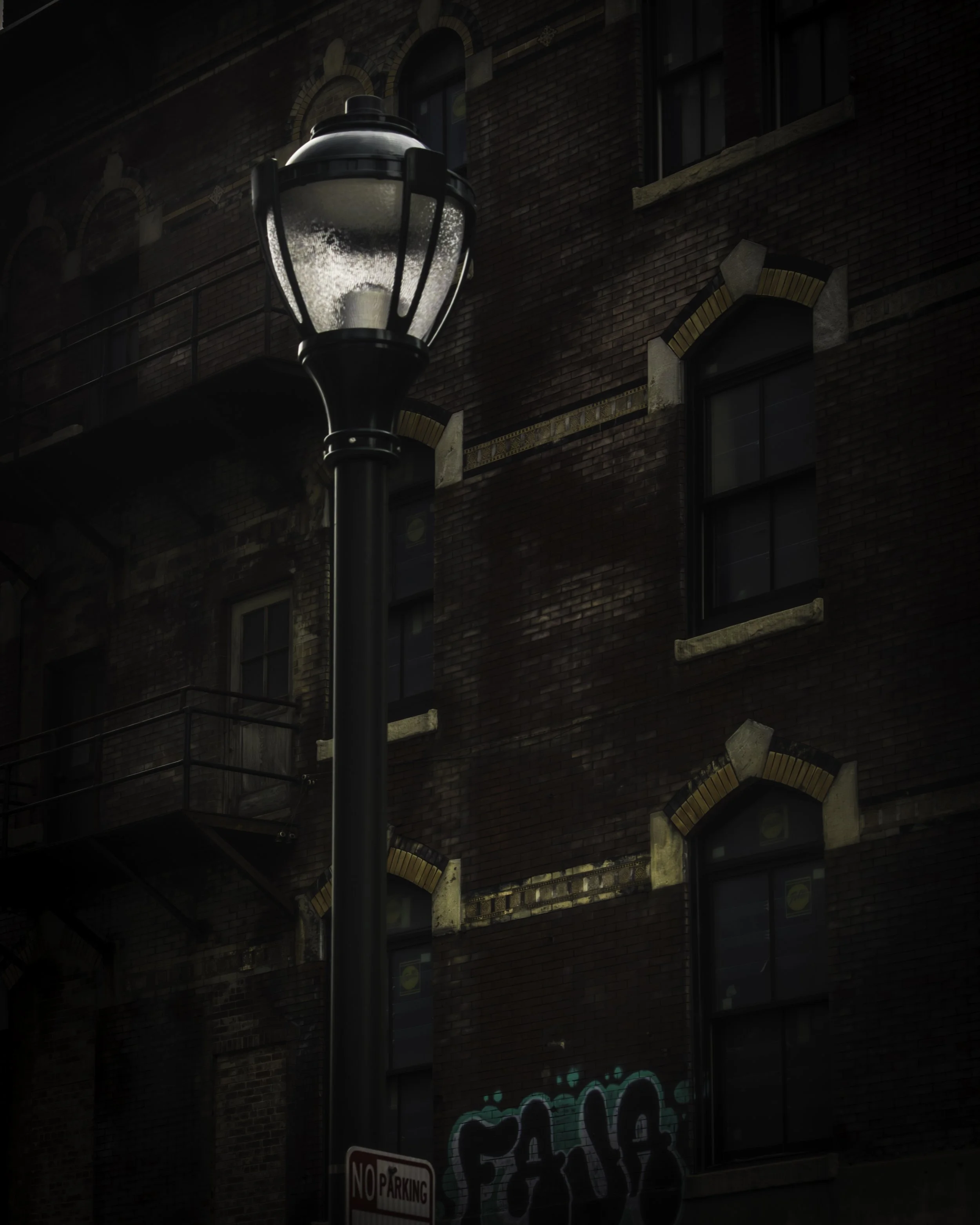 Arches in Shadow
Streetlamp glows against a dark brick building in downtown Philadelphia, with arched window trim and graffiti near the base of the wall.