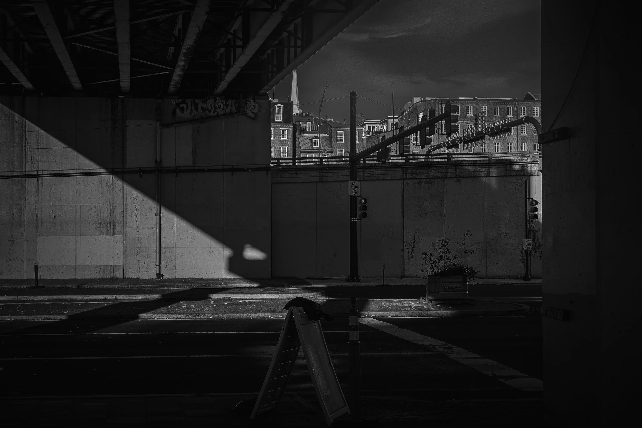 Underpass Geometry
Black and white city scene at Vine Street Expressway and Delaware Avenue in Philadelphia, where a diagonal beam of light cuts across a dark intersection and concrete walls.