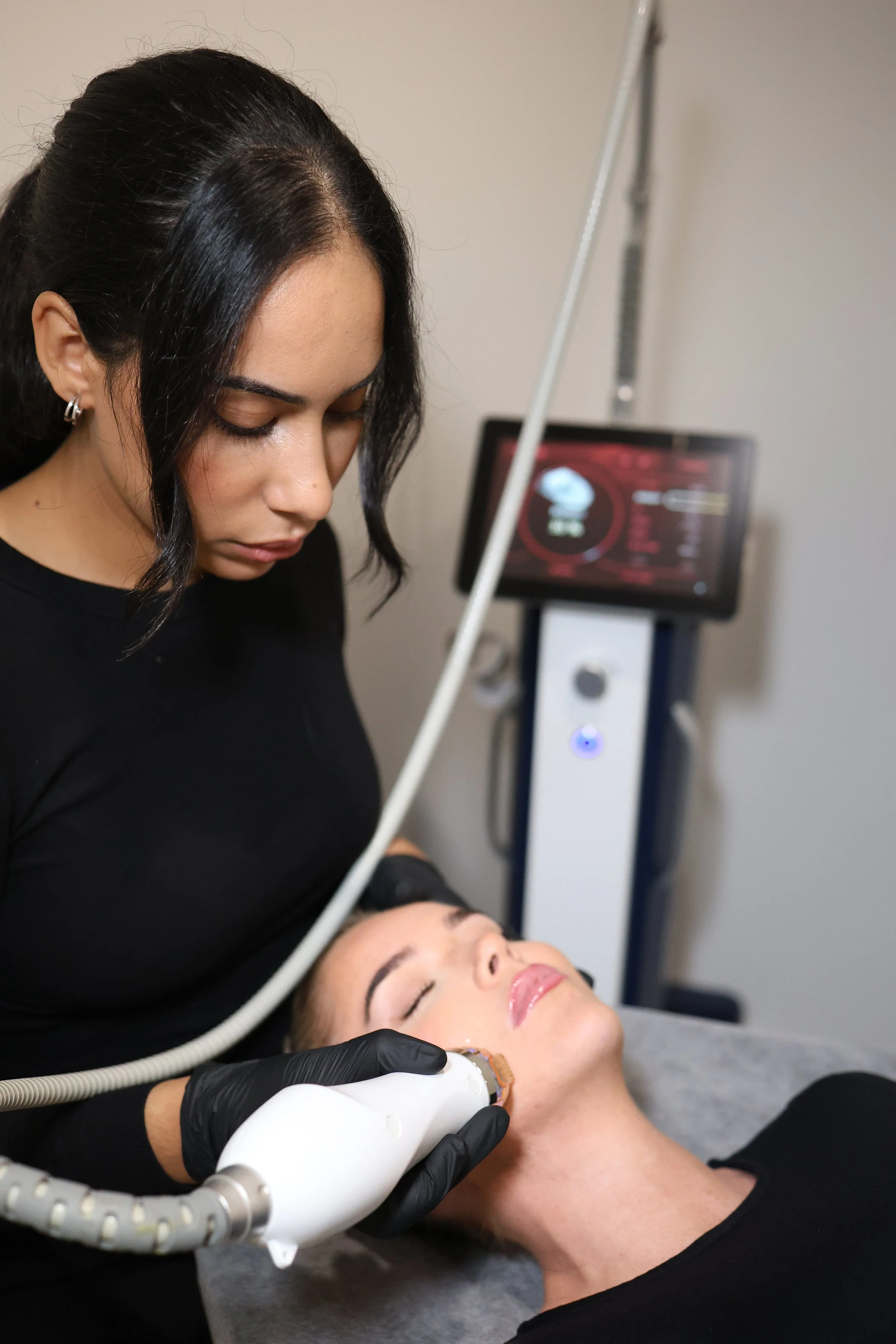 Close-up of a woman receiving a facial treatment with a laser device on her cheek.