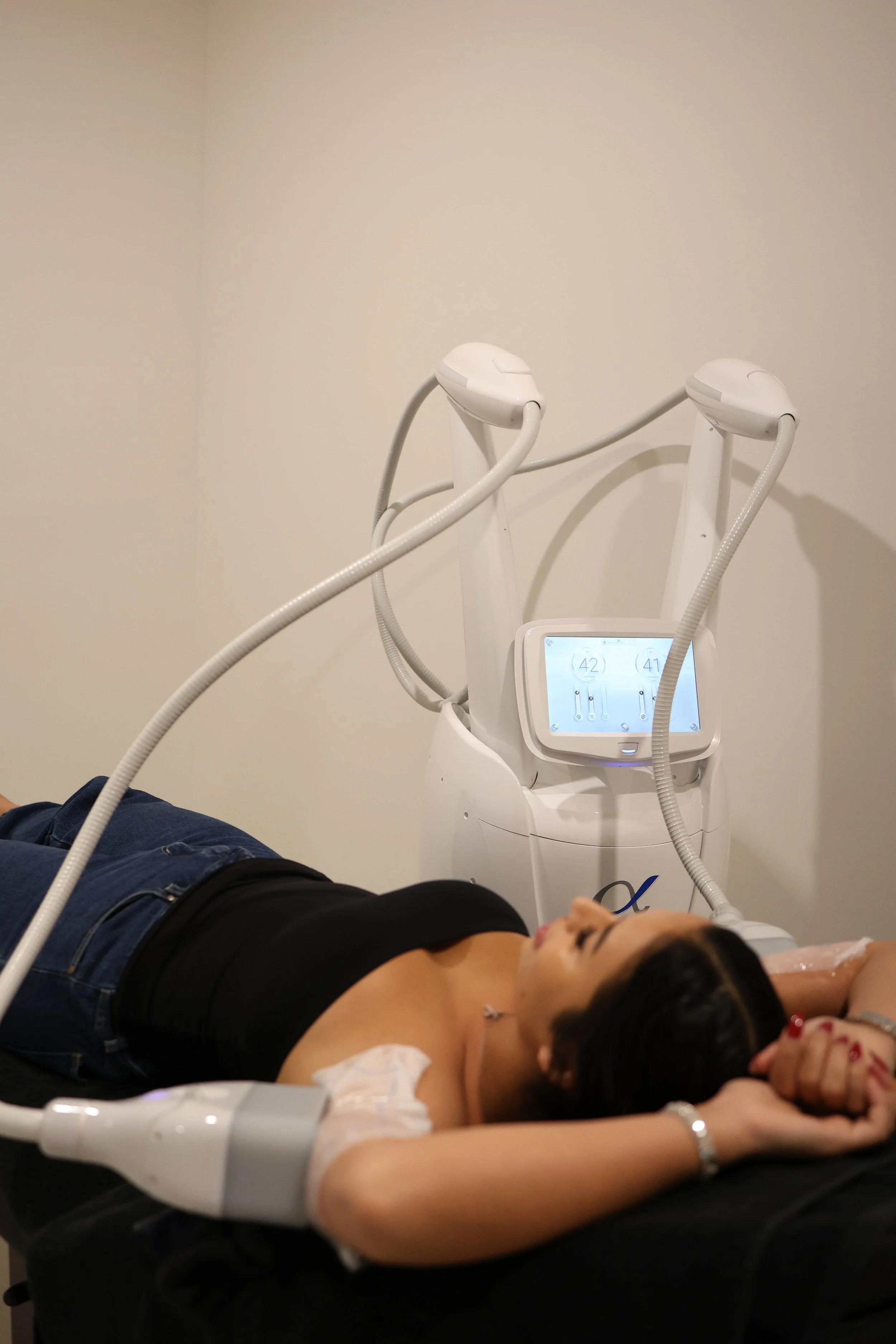 A woman undergoing a dermatological laser treatment, lying on a chair with a laser device near her chin in a medical clinic.