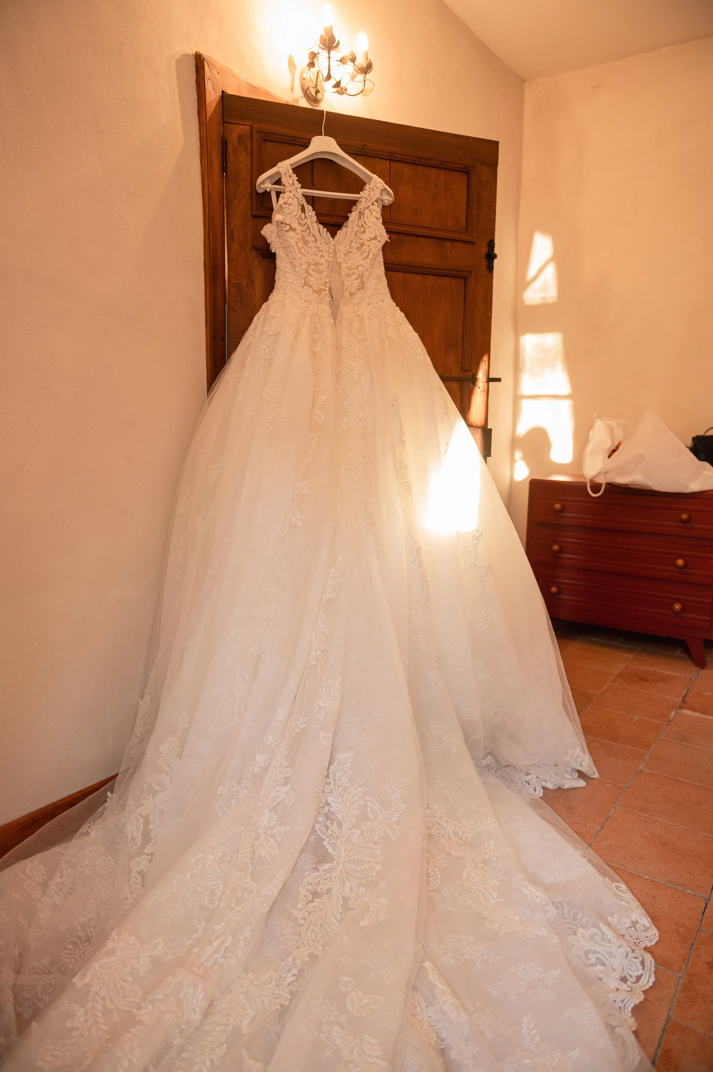 Robe de mariage blanche en dentelle suspendue à un crochet, dans une pièce avec un éclairage chaud.