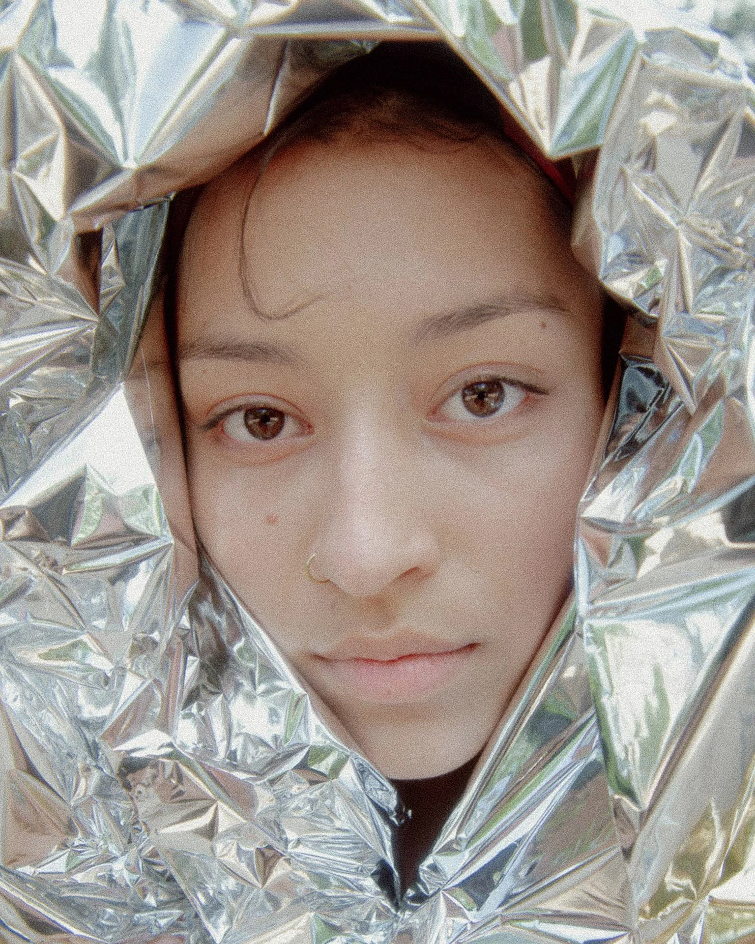 A person looking through crumpled aluminum foil, with wide eyes and a slight smile.