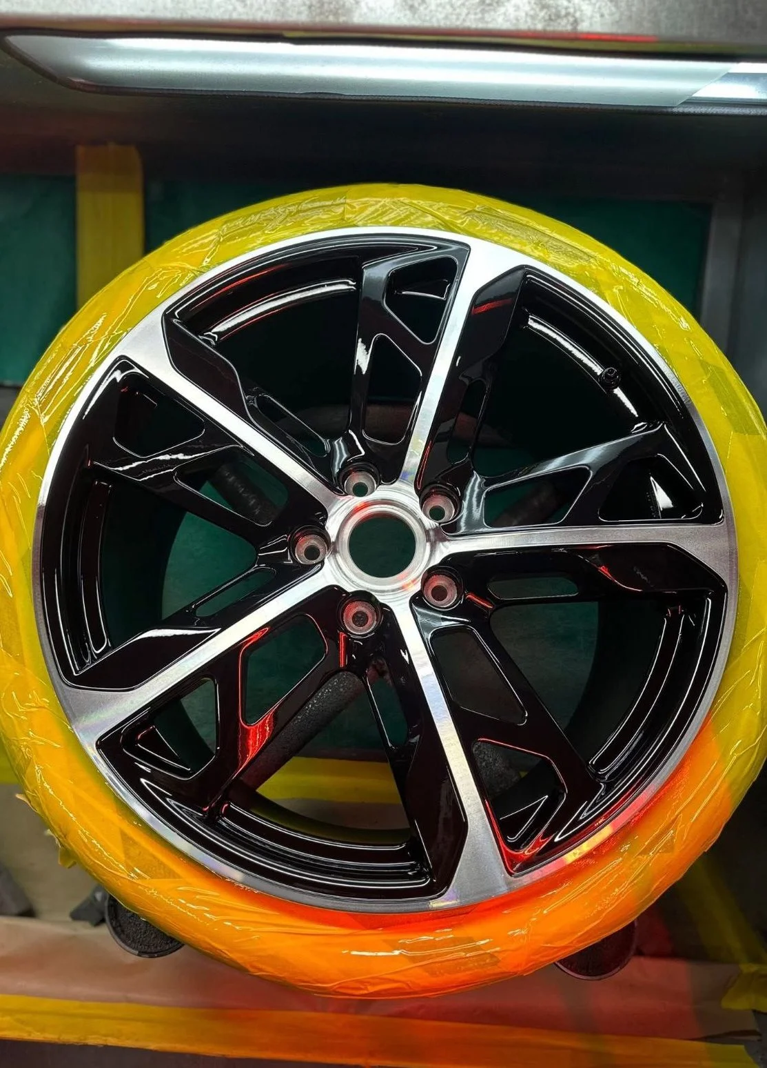 A car alloy with a black and diamond cut finish,  with the tyre wrapped in yellow plastic.