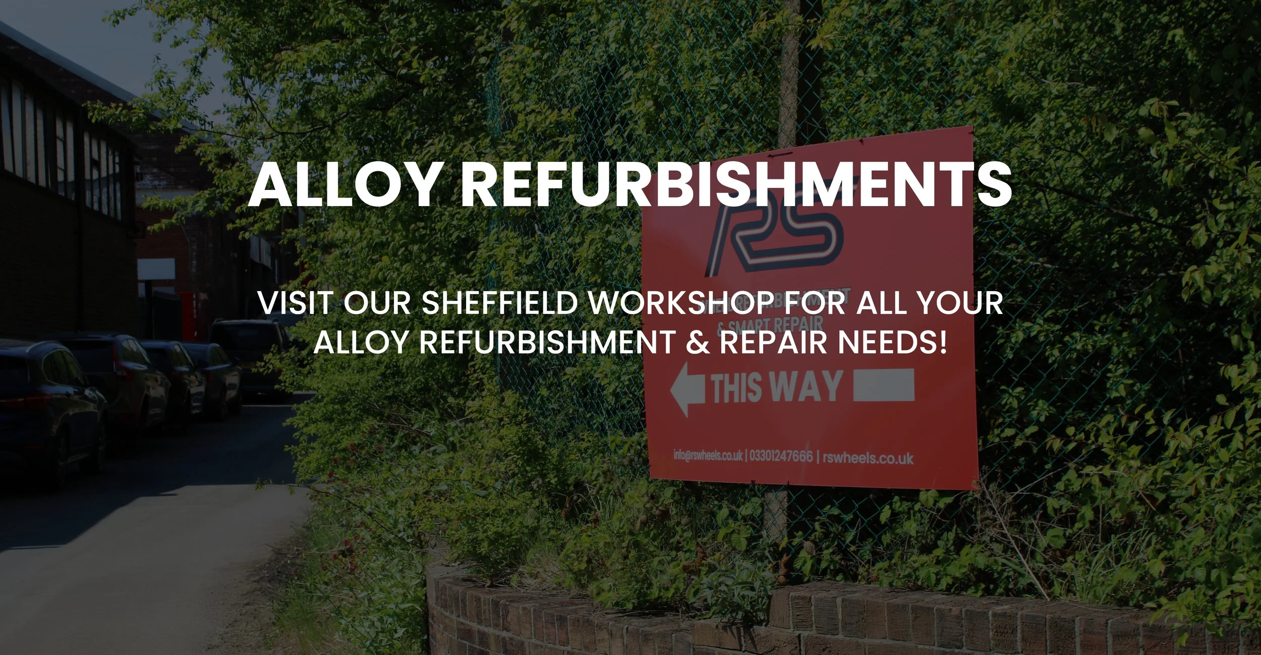 Red sign on a fence with the text 'RS WHEELS' and arrows, indicating the direction for alloy refurbishment and repair services in Sheffield, with cars parked alongside a building and trees in the background.