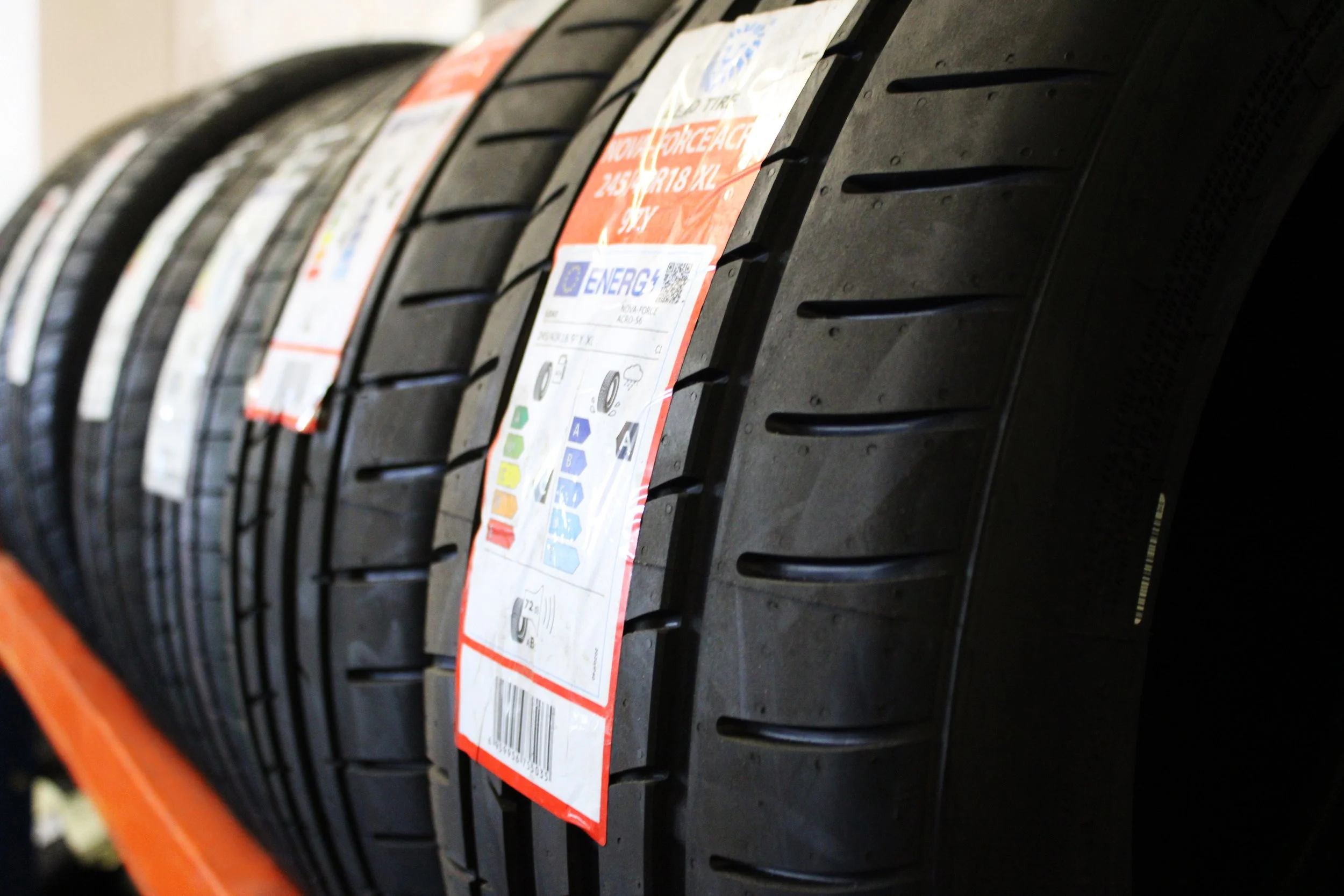 A close-up view of several new tires stacked horizontally, each with a colored and detailed informational label attached.