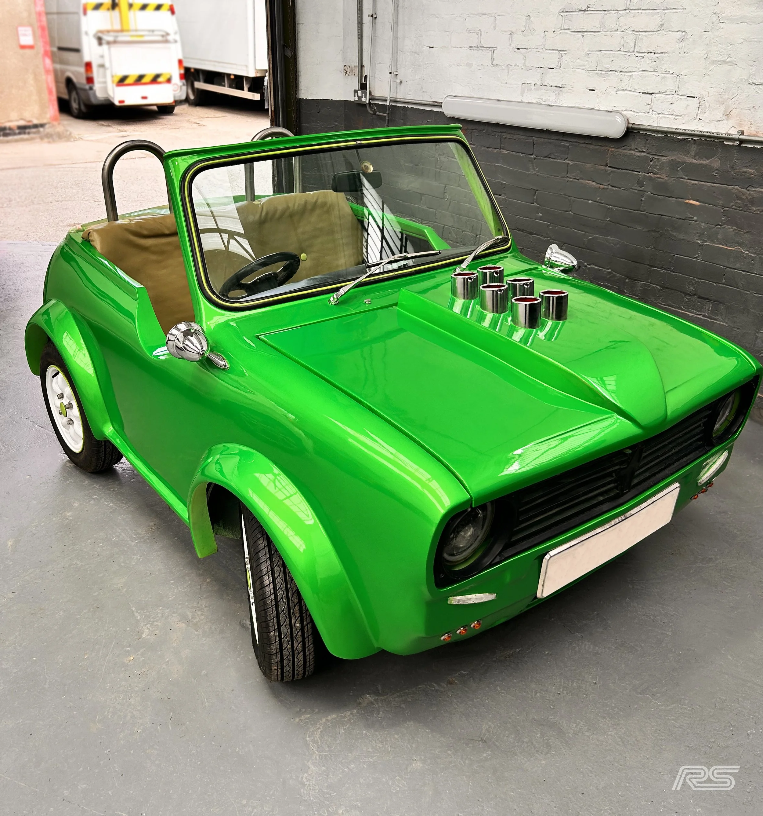 A small, bright green vintage-style Mini with a beige interior inside a paint workshop.