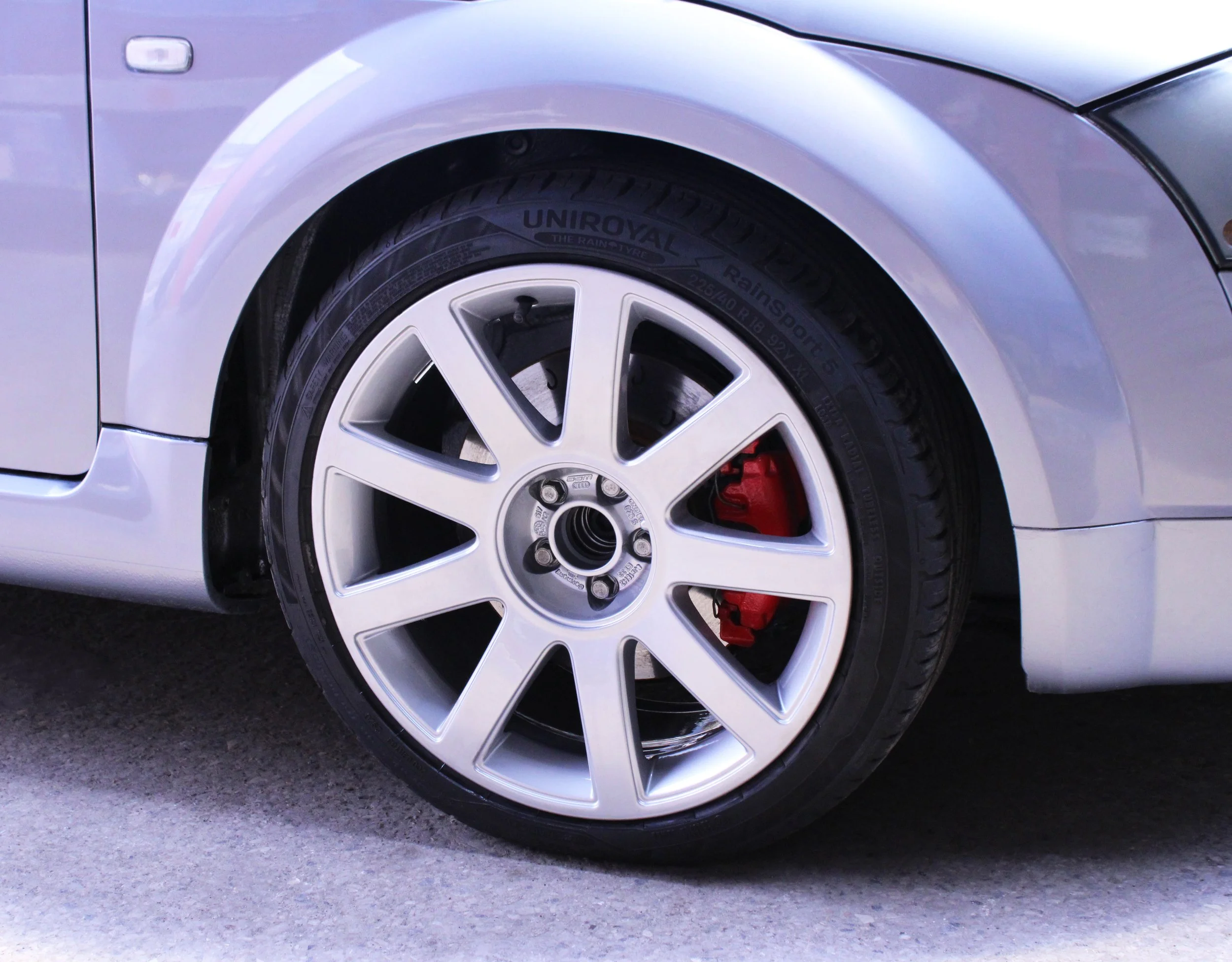 Close-up of a silver sports car's front wheel with a silver alloy after a powder coat refurbishment