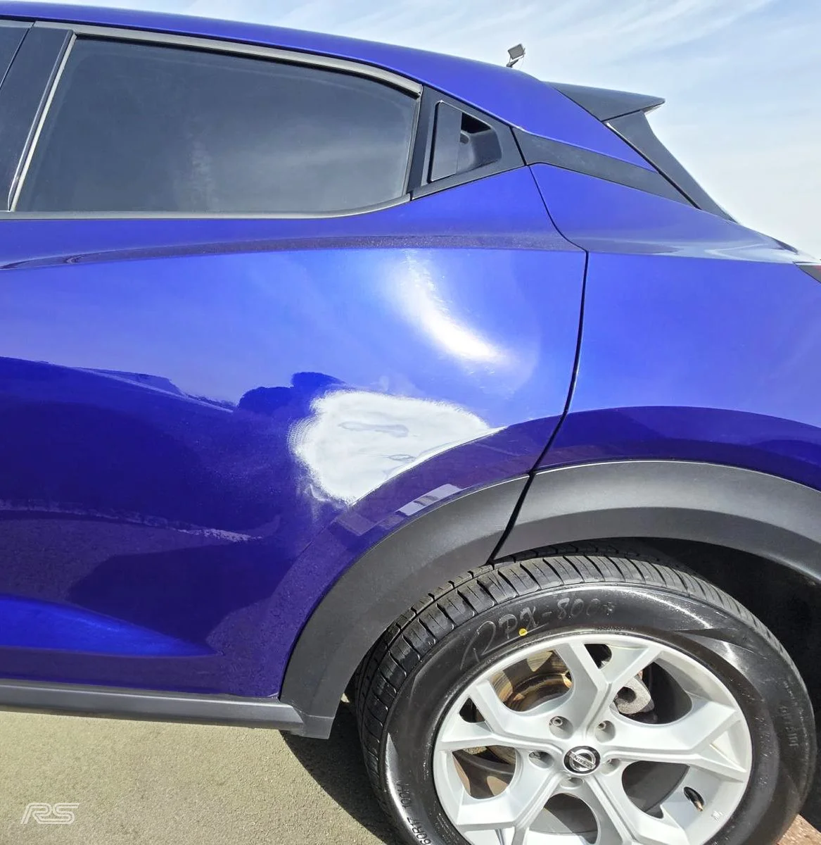 Close-up of a blue car's rear side showing the door and wheel, with damage clear on the surface.