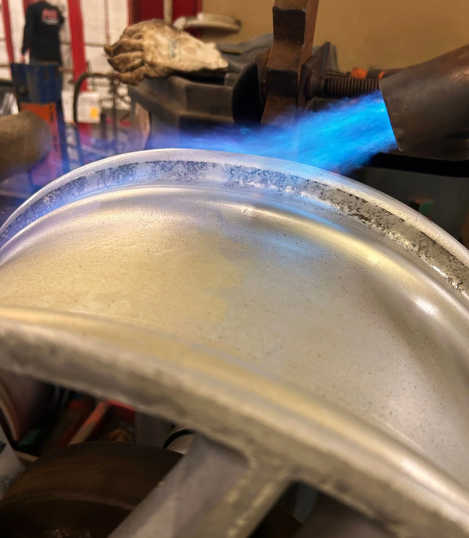 Close-up of a blow torch with a blue flame torch heating a wheel rim, in a workshop setting to repair a buckle in the wheel.