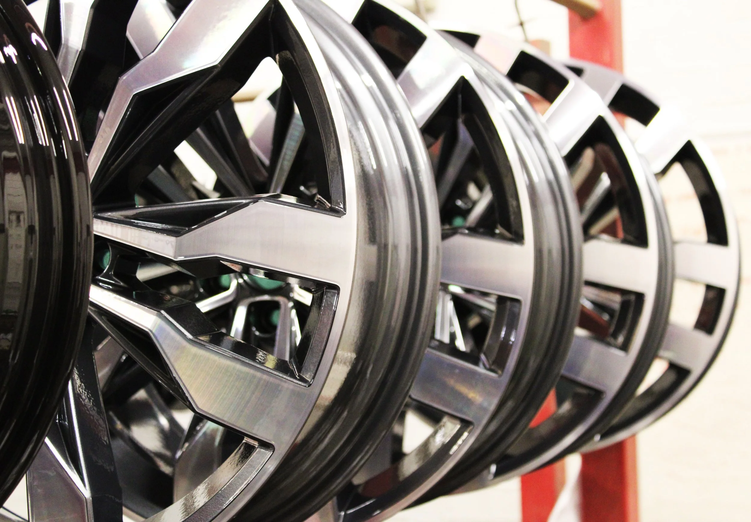 Close-up of several alloys with a silver and diamond cut finish, hanging in a workshop on a red metal rack.