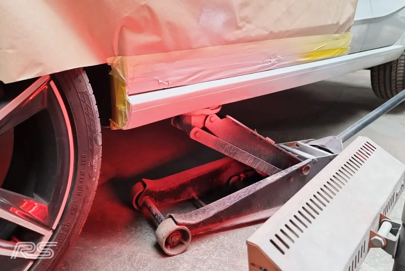 A car with bottom of a panel being repaired, and the glow of a heat lamp reflecting off the surface.
