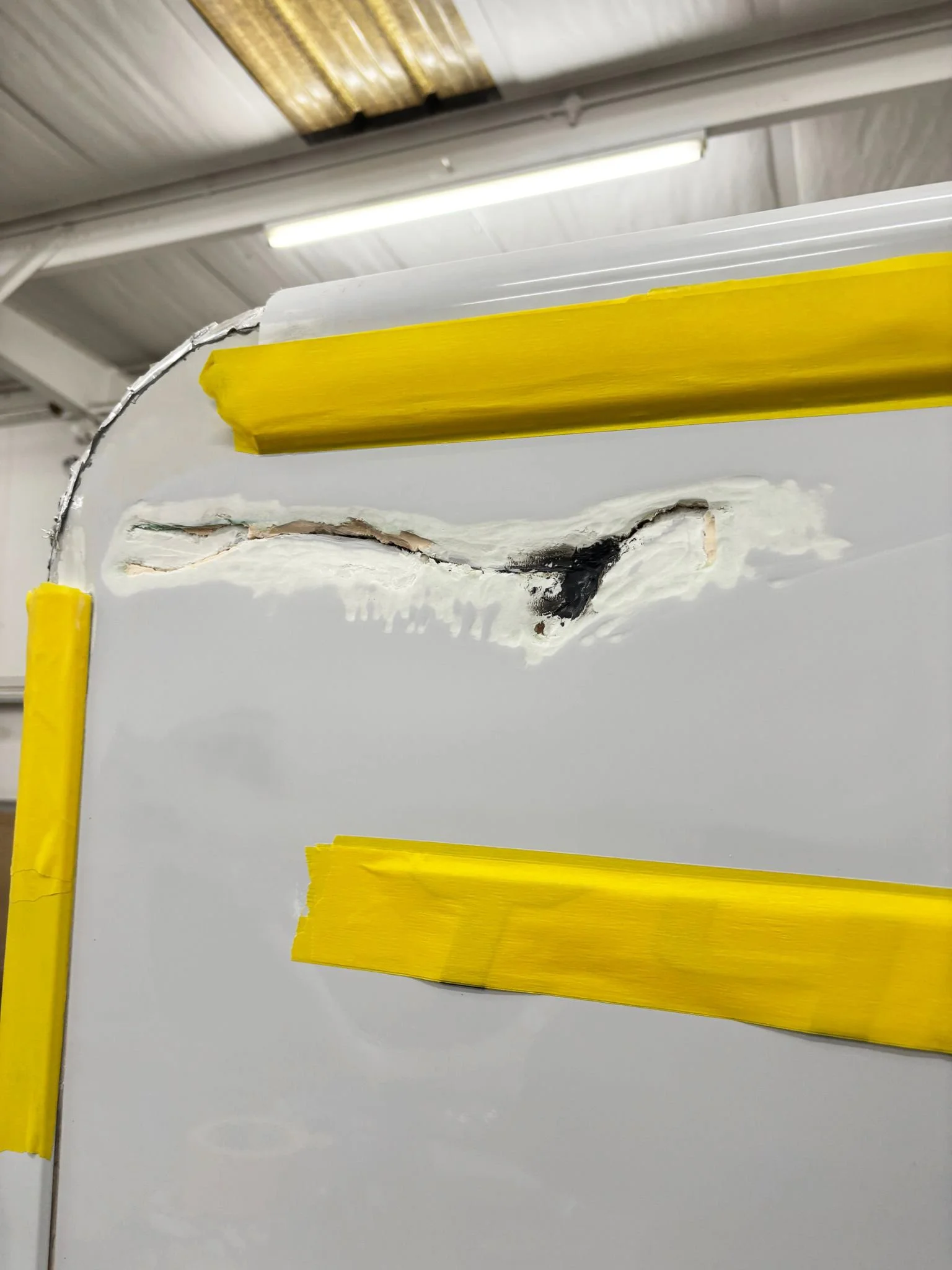 A damaged white surface on a motorhome with a large visible crack , covered partially with yellow painter's tape mid repair.