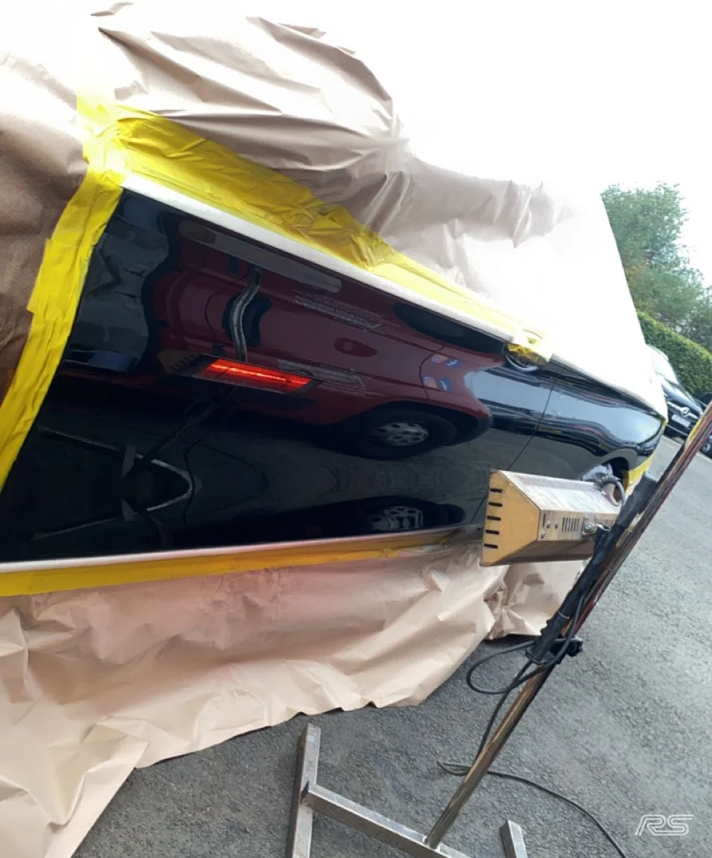 Car undergoing a paint repair or coating process, covered with protective paper and masking tape.