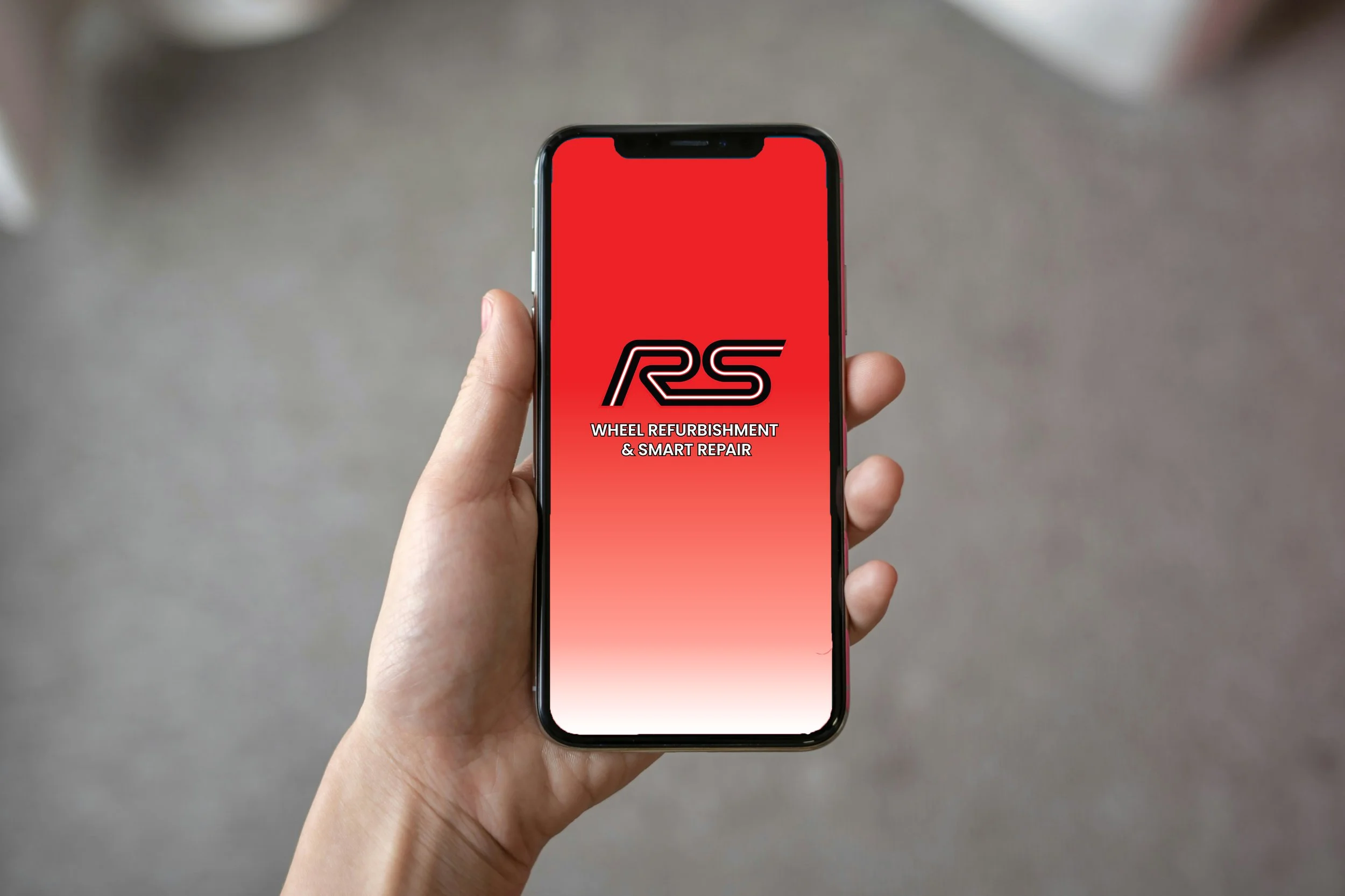 A hand holding a smartphone displaying a logo for RS Wheel Refurbishment & Smart Repair on a red gradient background.
