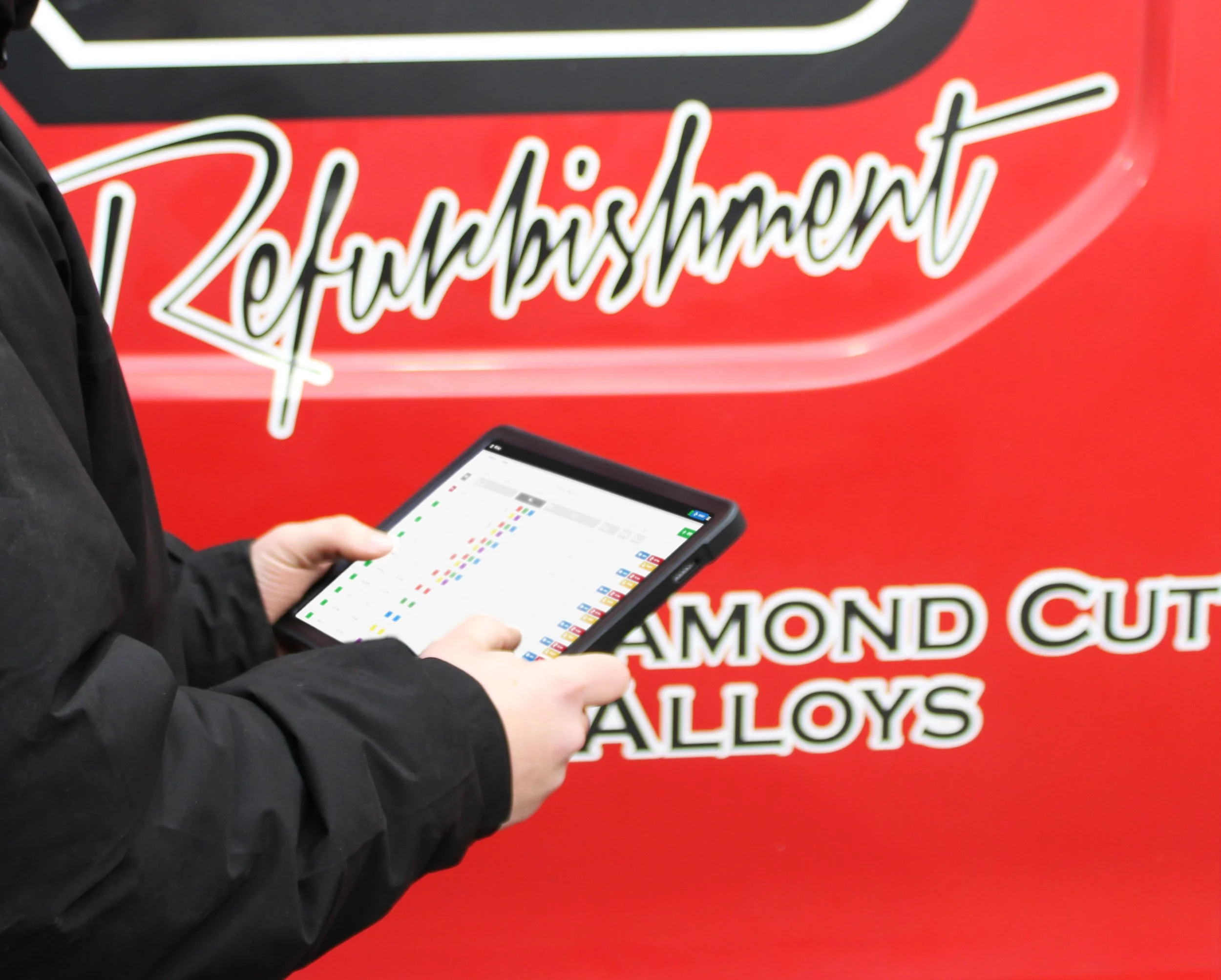 Manager with black jacket, completing onsite check in front of a red RS wheels van using a tablet with the RSW hub onscreen