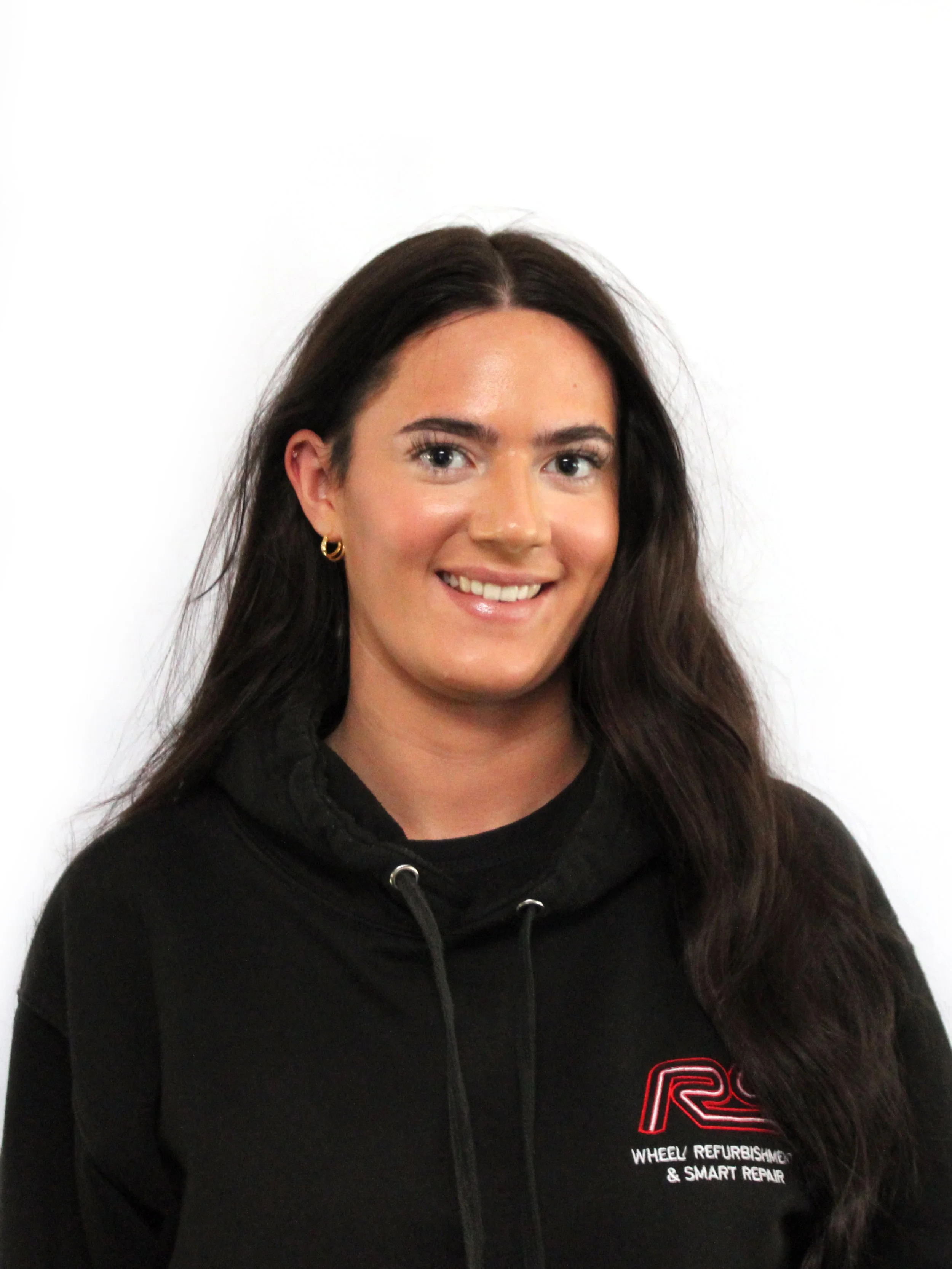 A young woman with long dark hair, smiling, wearing a black hoodie with a logo and text that reads 'Wheel Refurbishment & Smart Repair'.