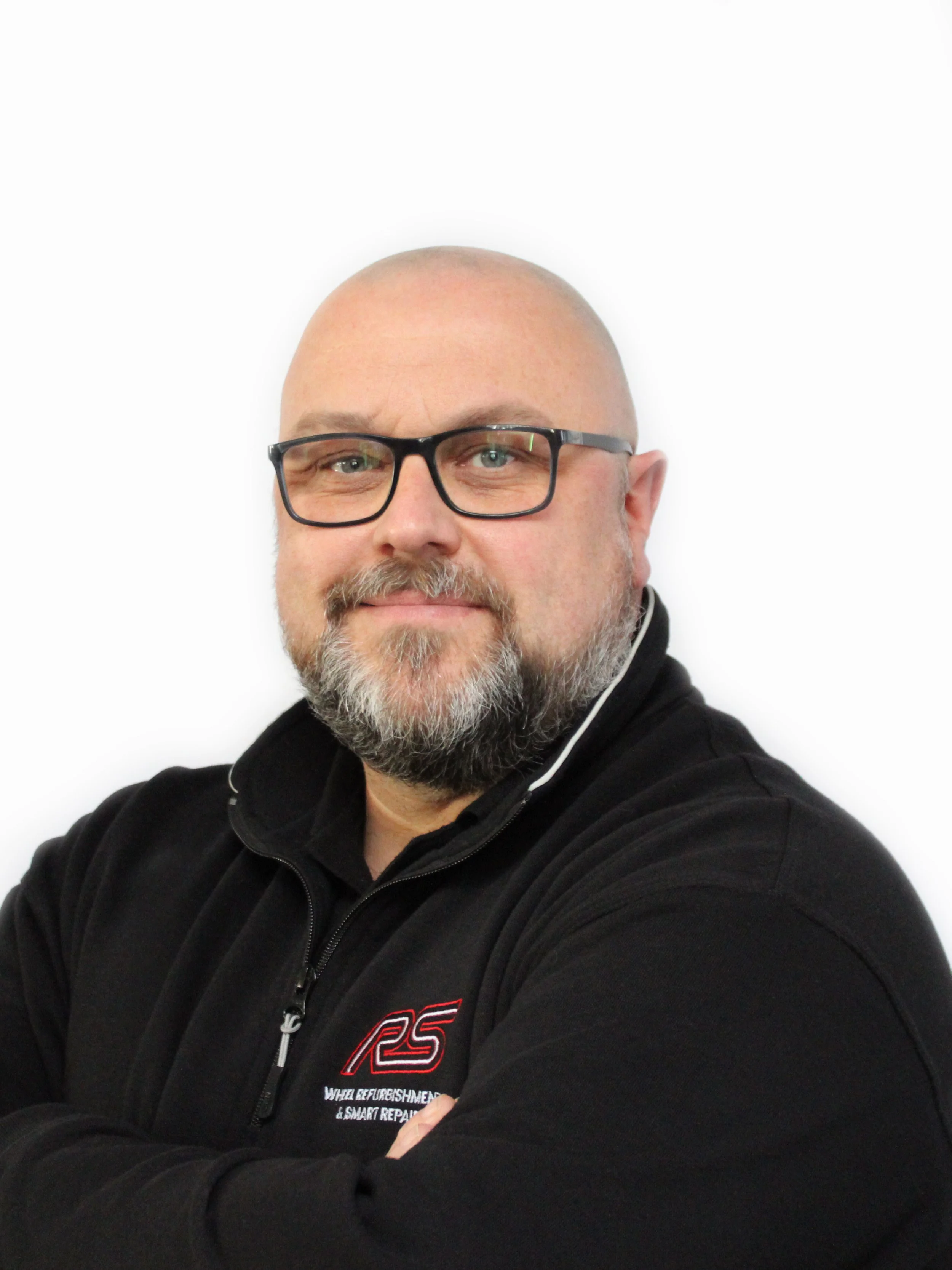 Bald man with glasses and a beard, wearing a black jacket with a logo, posing against a white background.