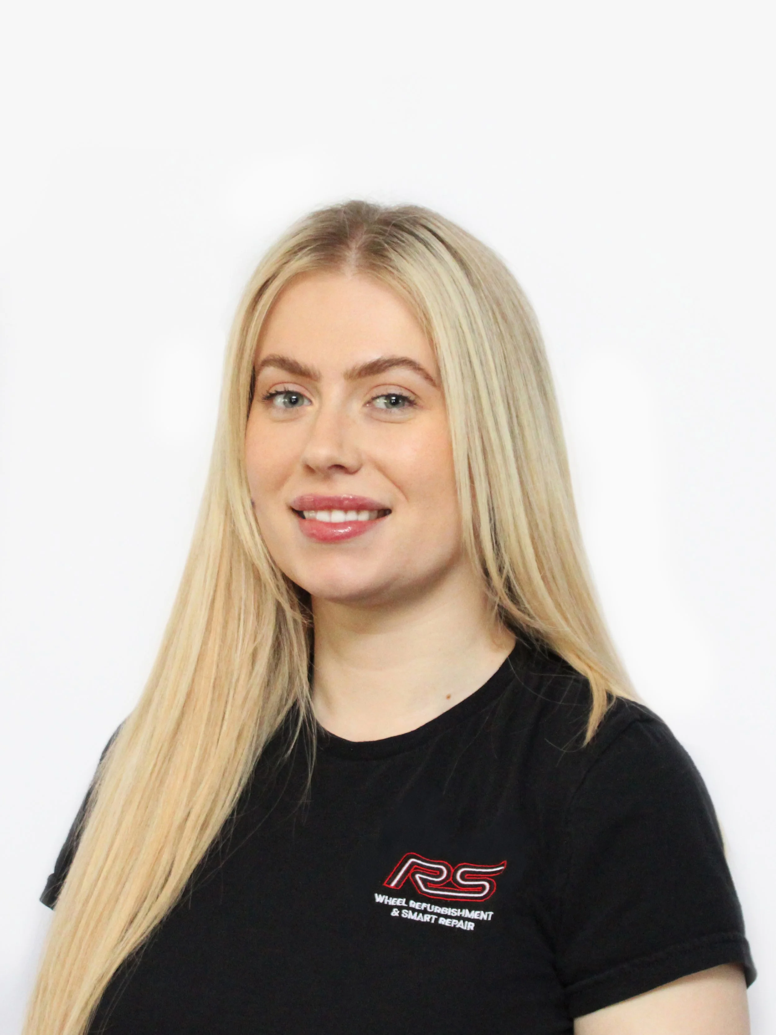 A young woman with long blonde hair, wearing a black t-shirt with a logo that reads 'RS Wheel Refurbishment & Smart Repair,' smiling against a plain white background.