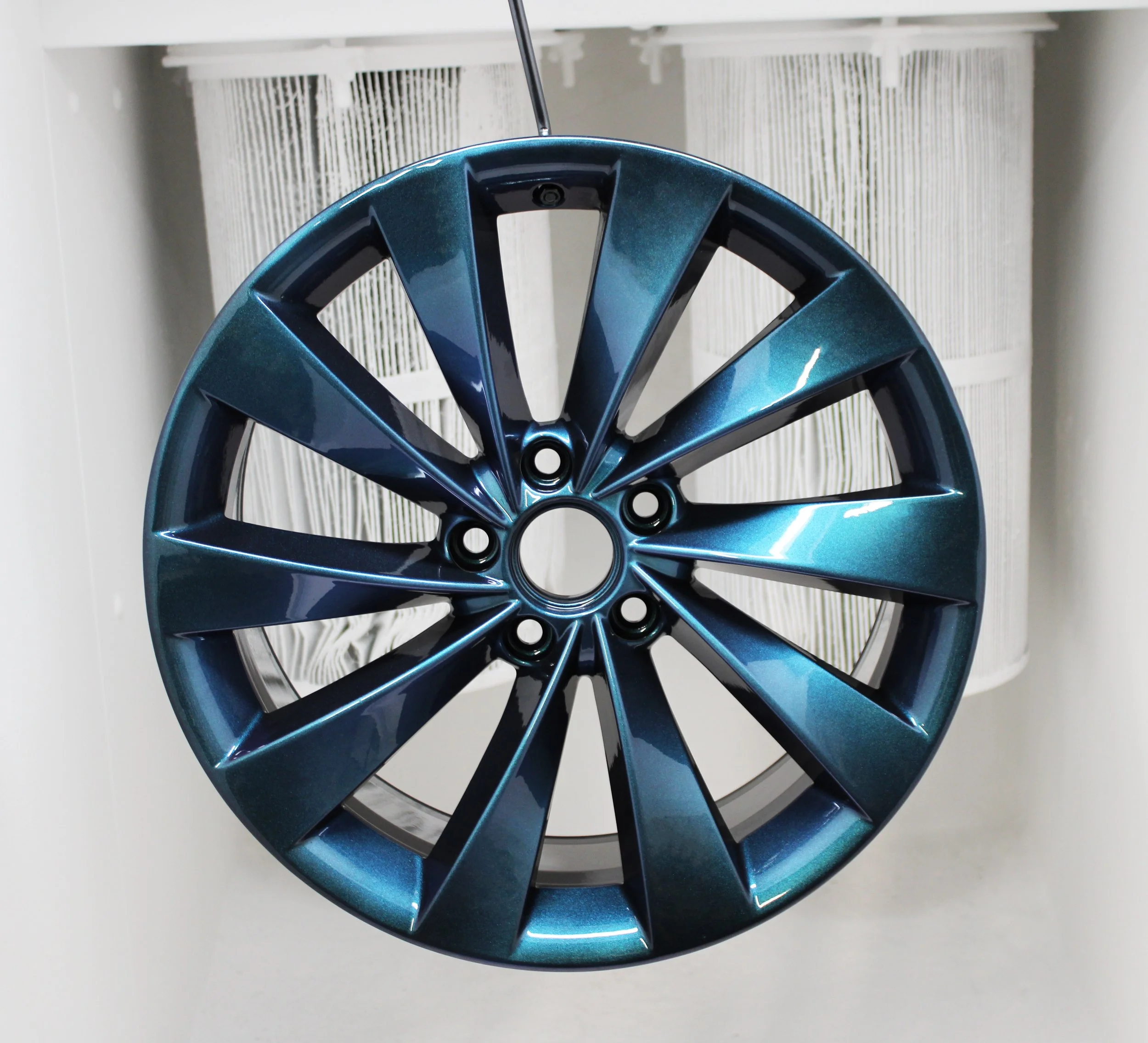 A wheel hung up in a powdercoating booth with a bespoke colour on
