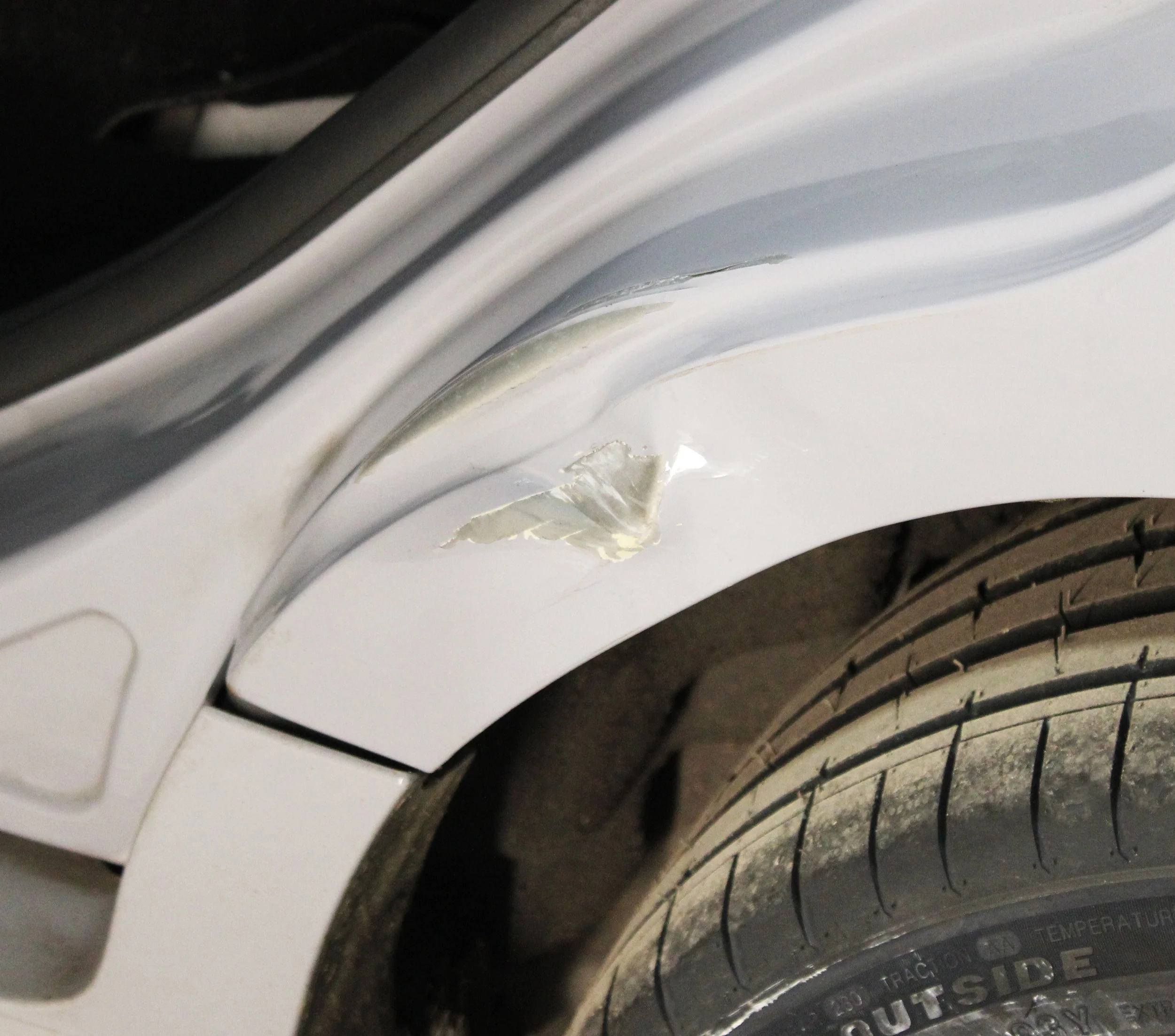 Close-up of a car with a torn section on the car's fender near the wheel.