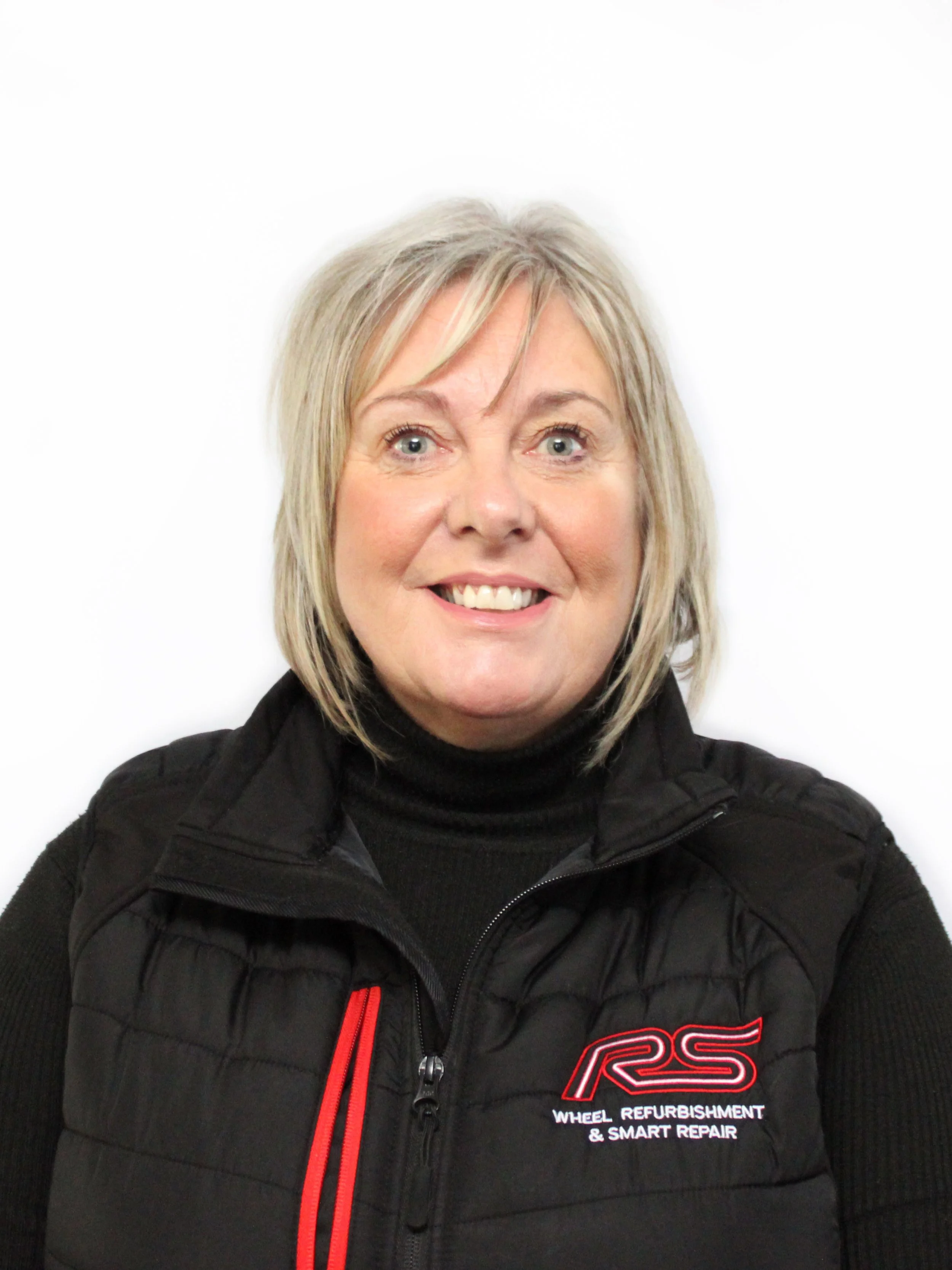 A woman with shoulder-length blonde hair, smiling, wearing a black jacket with an 'RS Wheel Refurbishment & Smart Repair' logo on the chest, against a plain white background.