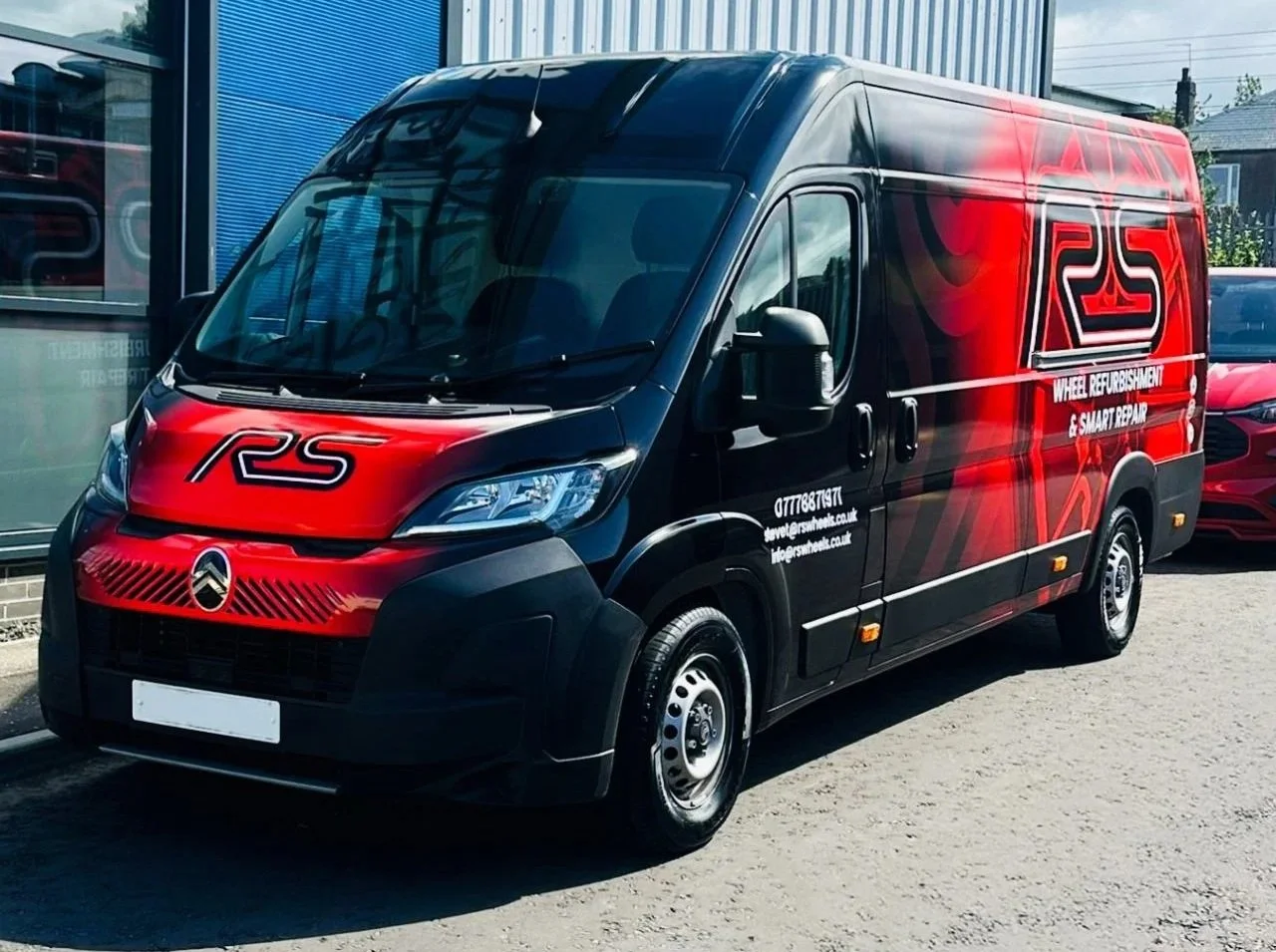 Black and red commercial van with a large 'RS' logo and text for wheel refurbishing and smart repair services, parked outside a building.