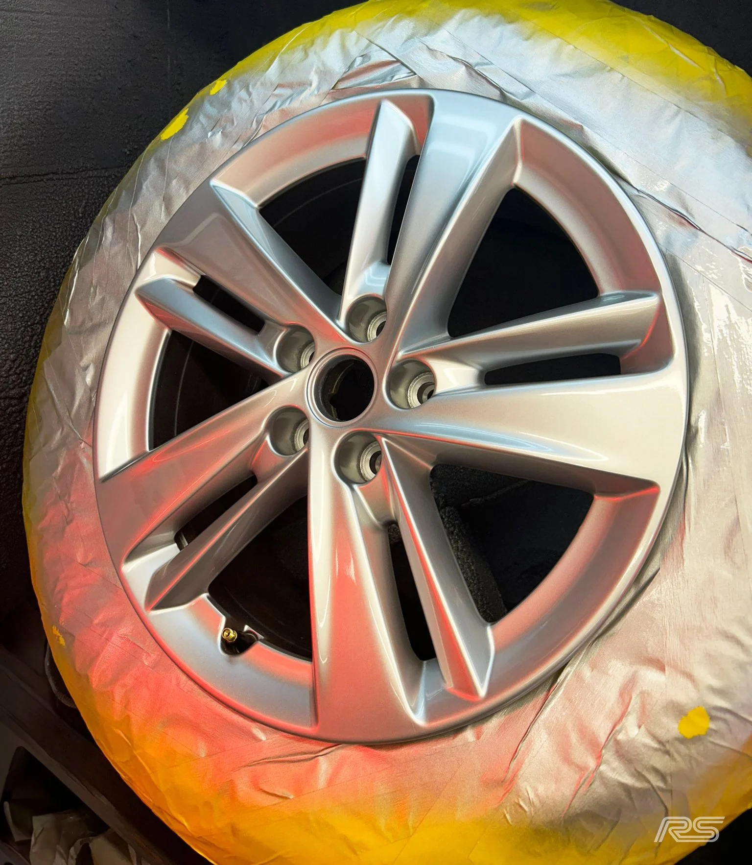 A silver alloy wheel with tape on the tyre, painted silver.