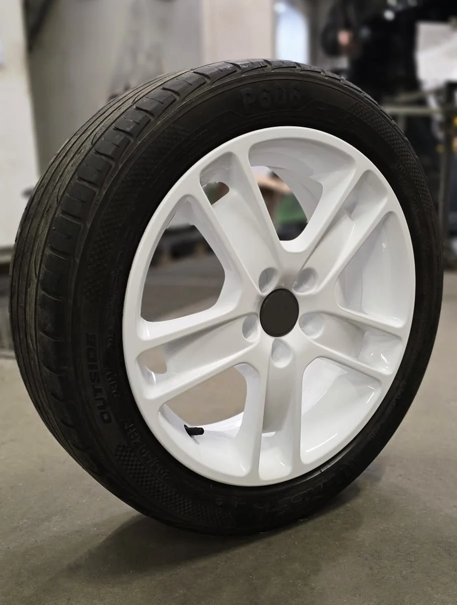 A close-up of a black tyre mounted on a white alloy, set against a blurred workshop background.