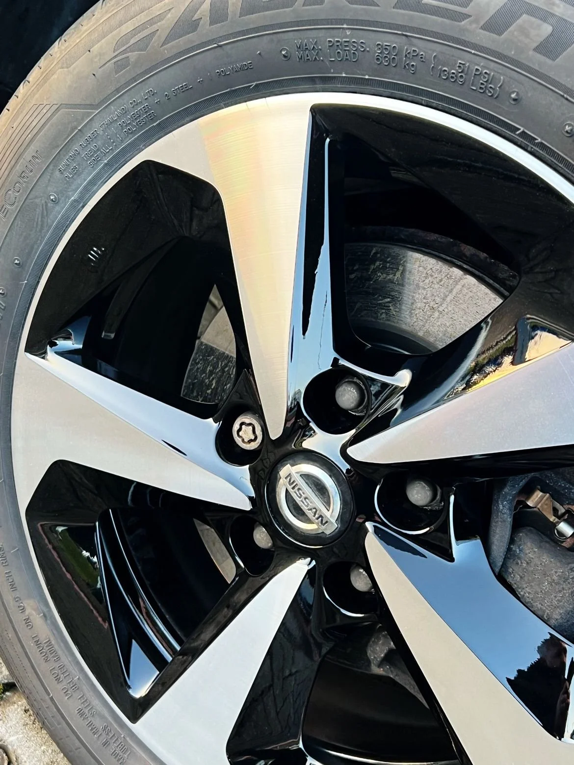 Close-up of a black and diamond cut Nissan alloy wheel with a tyre mounted on it.
