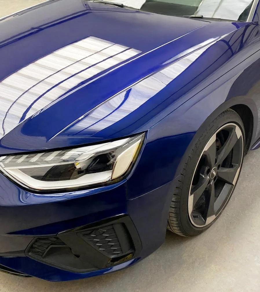 Close-up of a blue sports car's front left side, showing the headlight, wheel, and part of the front bumper.