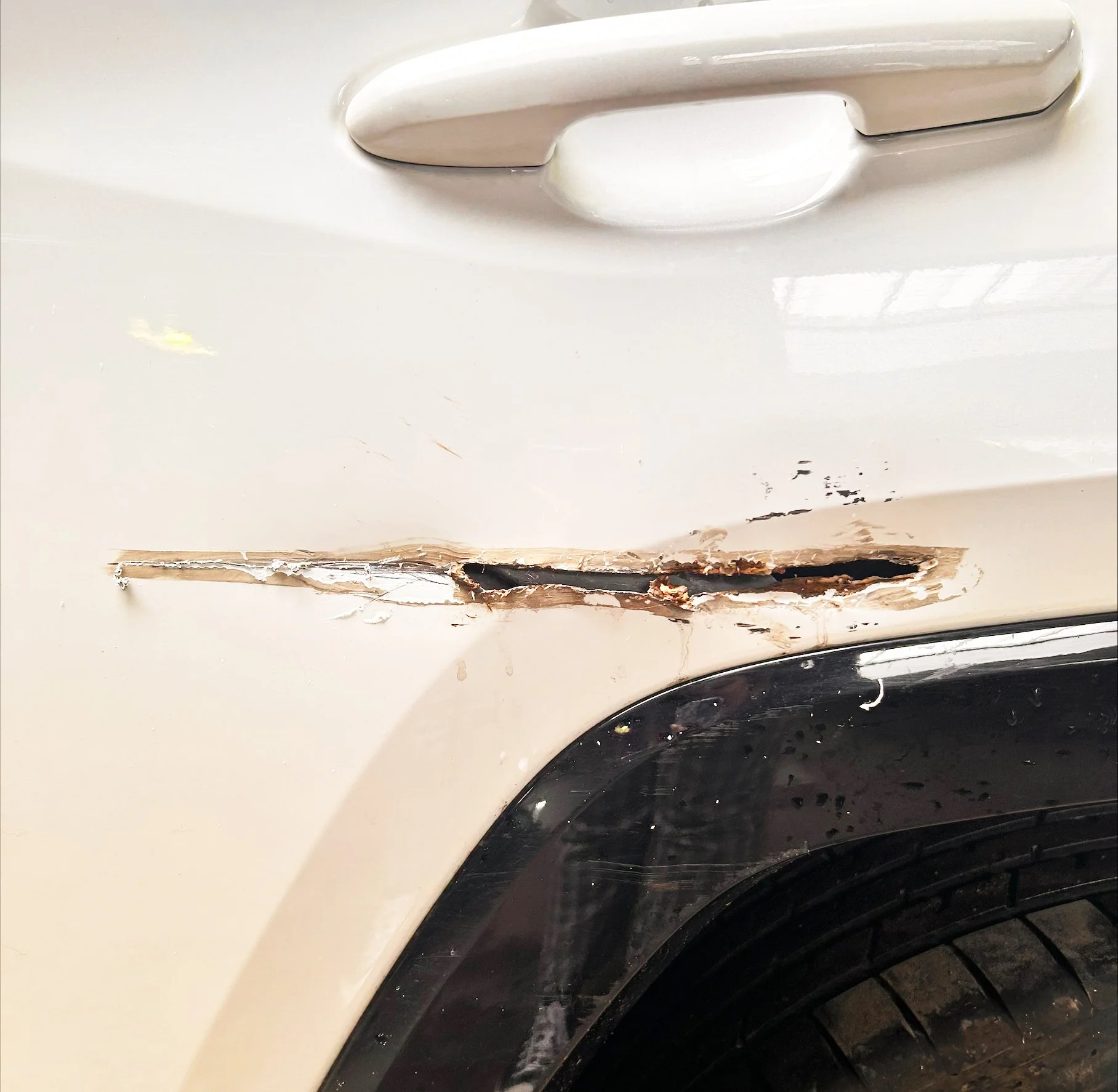 Close-up of a white car showing a long scratch and damage near the wheel well.