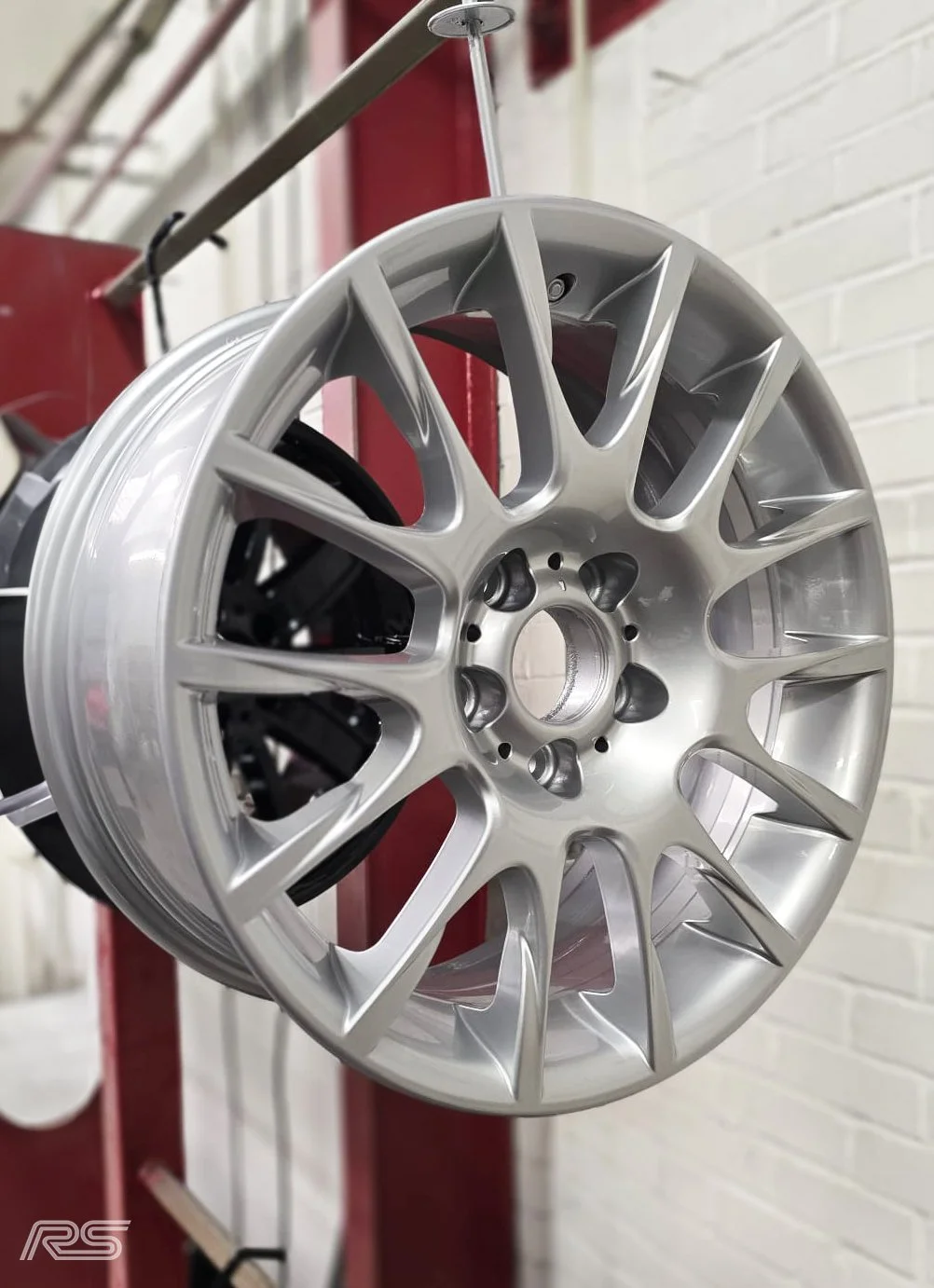 A silver alloy wheel rim hanging on a hook in a workshop.