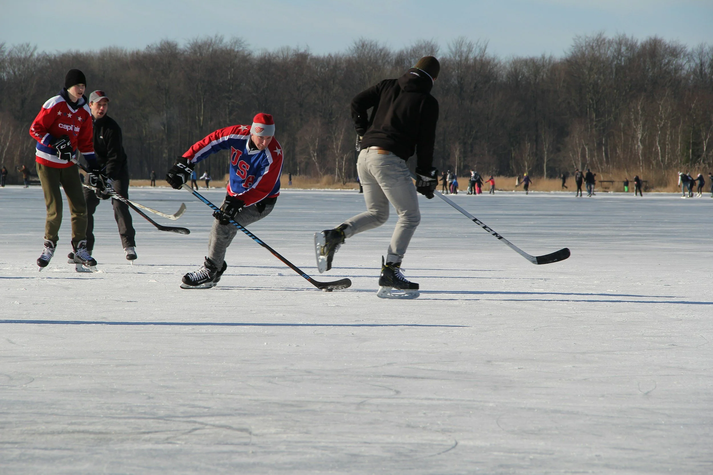 People playing hockey on an outdoor ice rink during winter, with some wearing team jerseys and winter clothing.