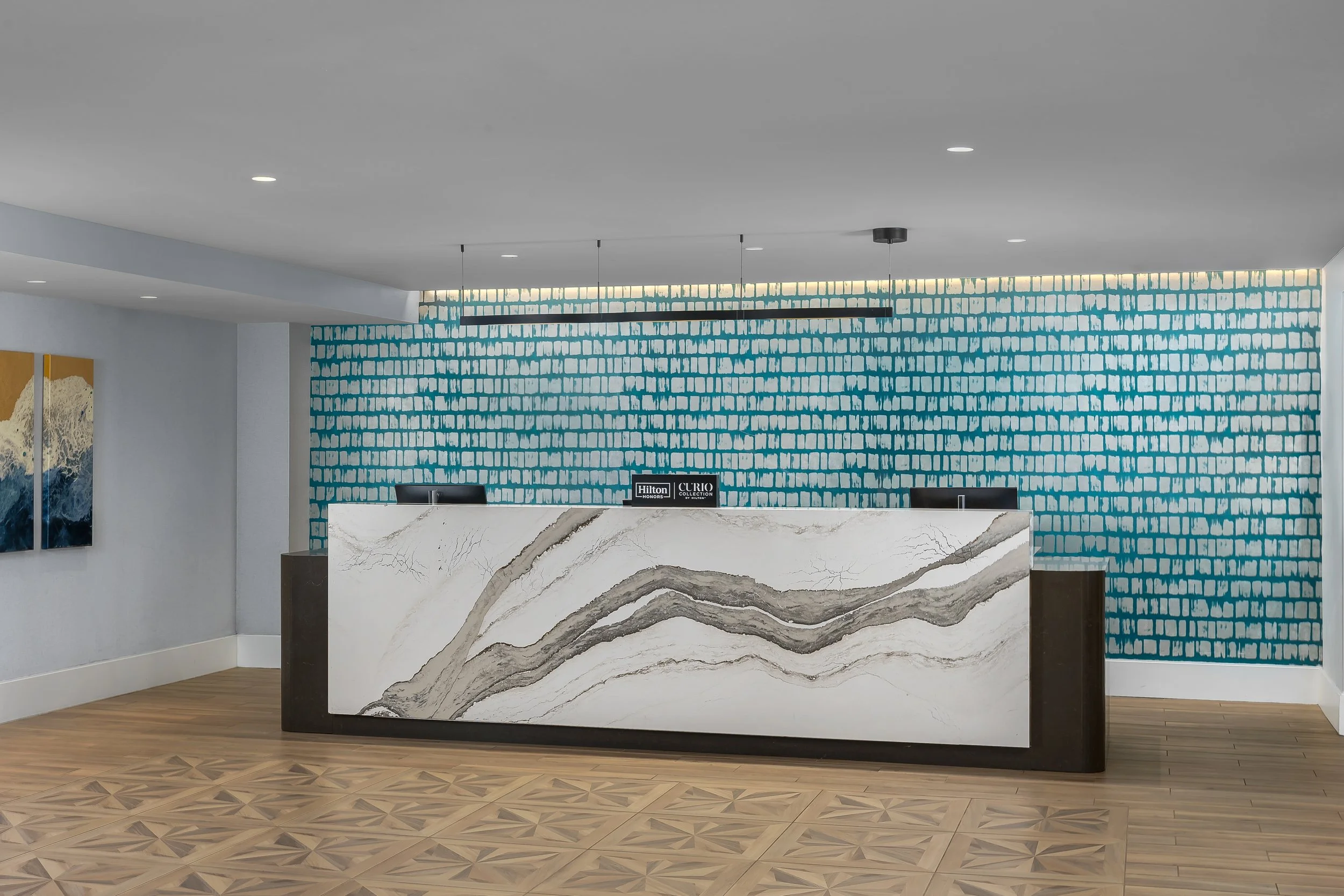 Hotel reception desk with a large white marble countertop with brown and gray veining, set against a blue patterned wall and a white ceiling with recessed lighting.