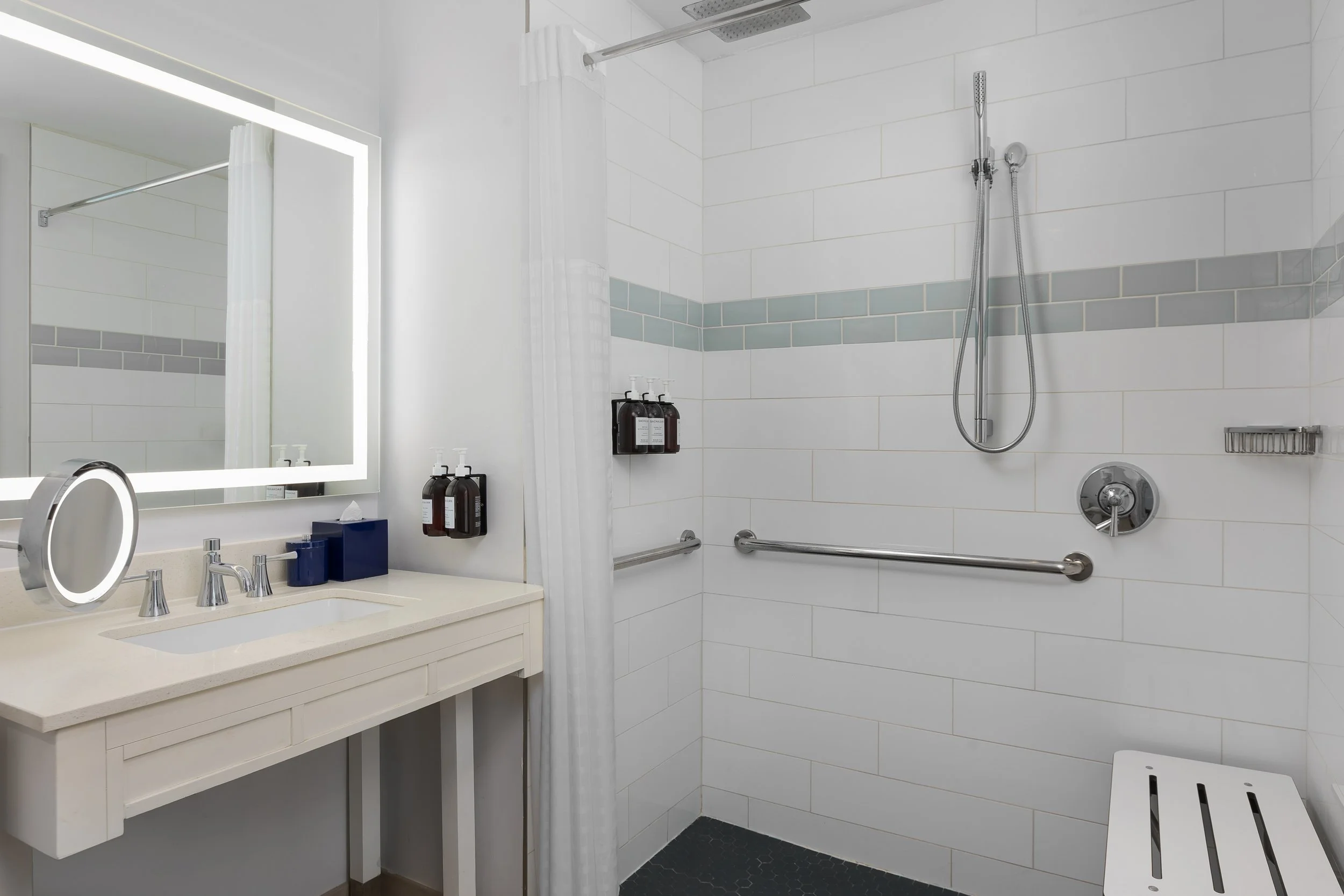 Bright bathroom with a white vanity, large mirror with LED lighting, and a walk-in shower with a showerhead, handheld shower, and grab bars.