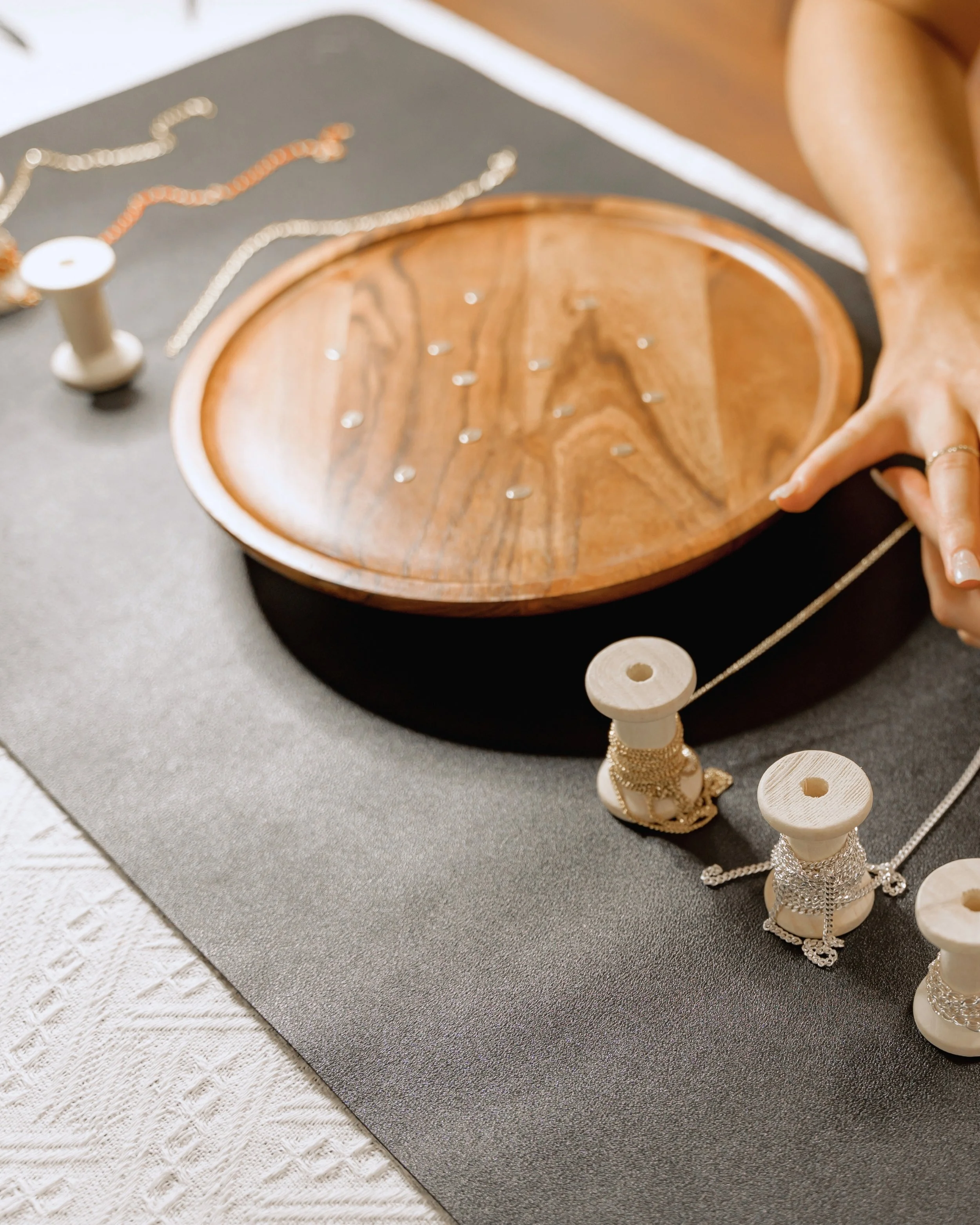 Several spools of gold and silver chains on a table, with a wooden dish in the middle holding tiny jewelry charms.