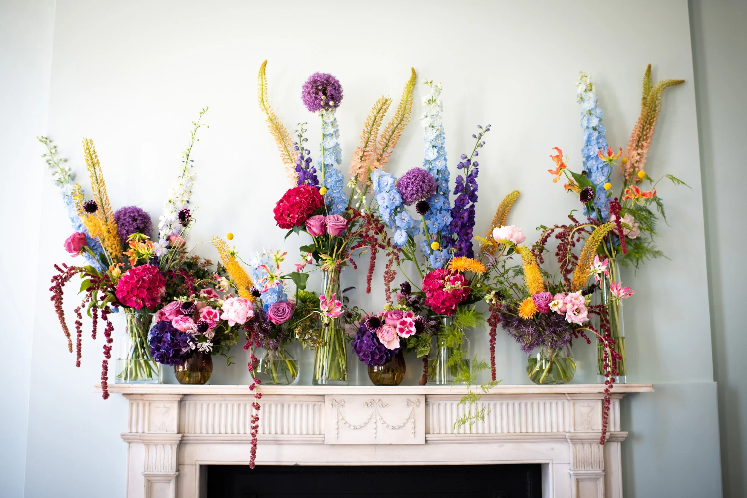 Arrangement of colorful flowers in glass vases on a fireplace mantel.