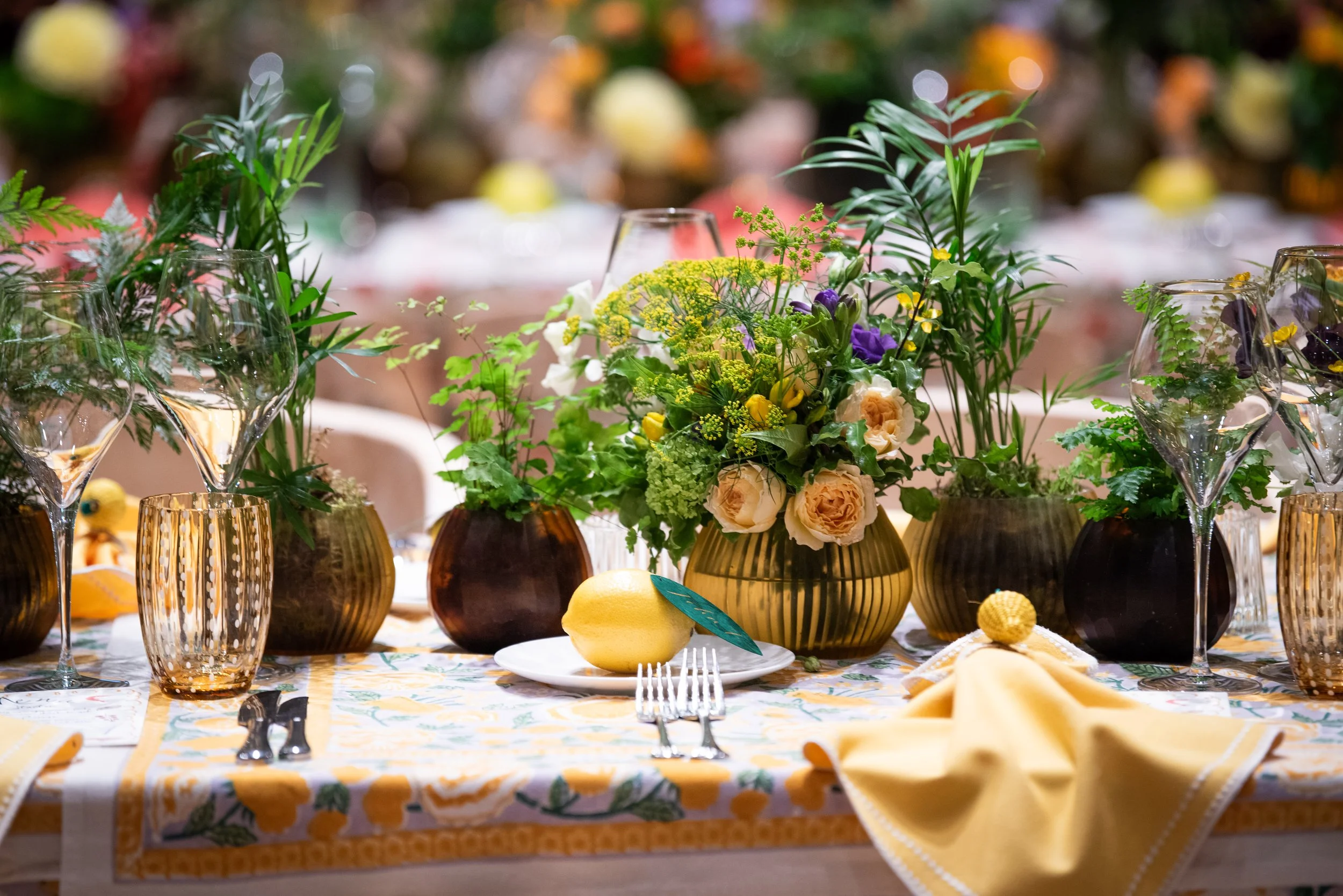 Table decorated with a floral centerpiece, surrounded by wine glasses and yellow napkins, set for a formal event.