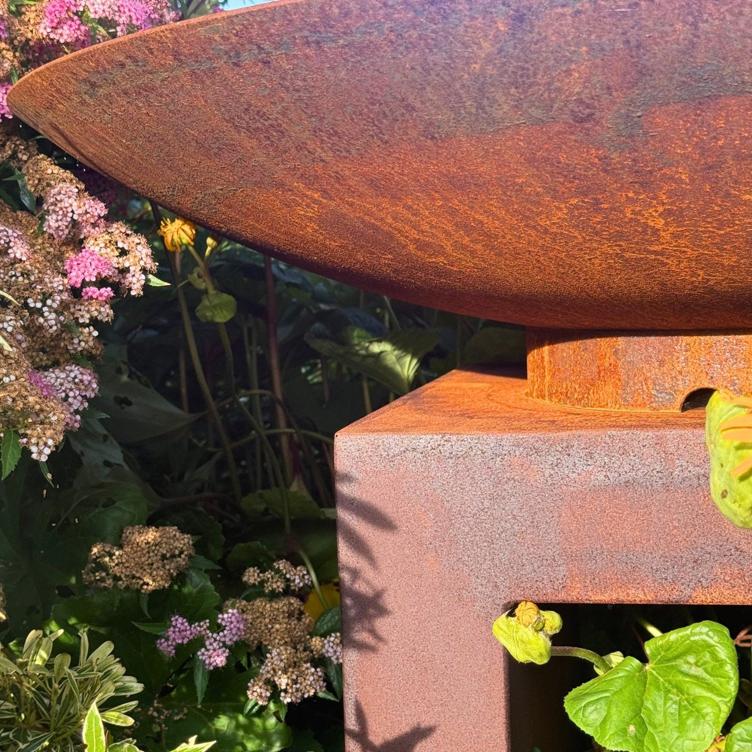 Close-up detail of a corten steel water bowl resting on its rust-patina pedestal base.