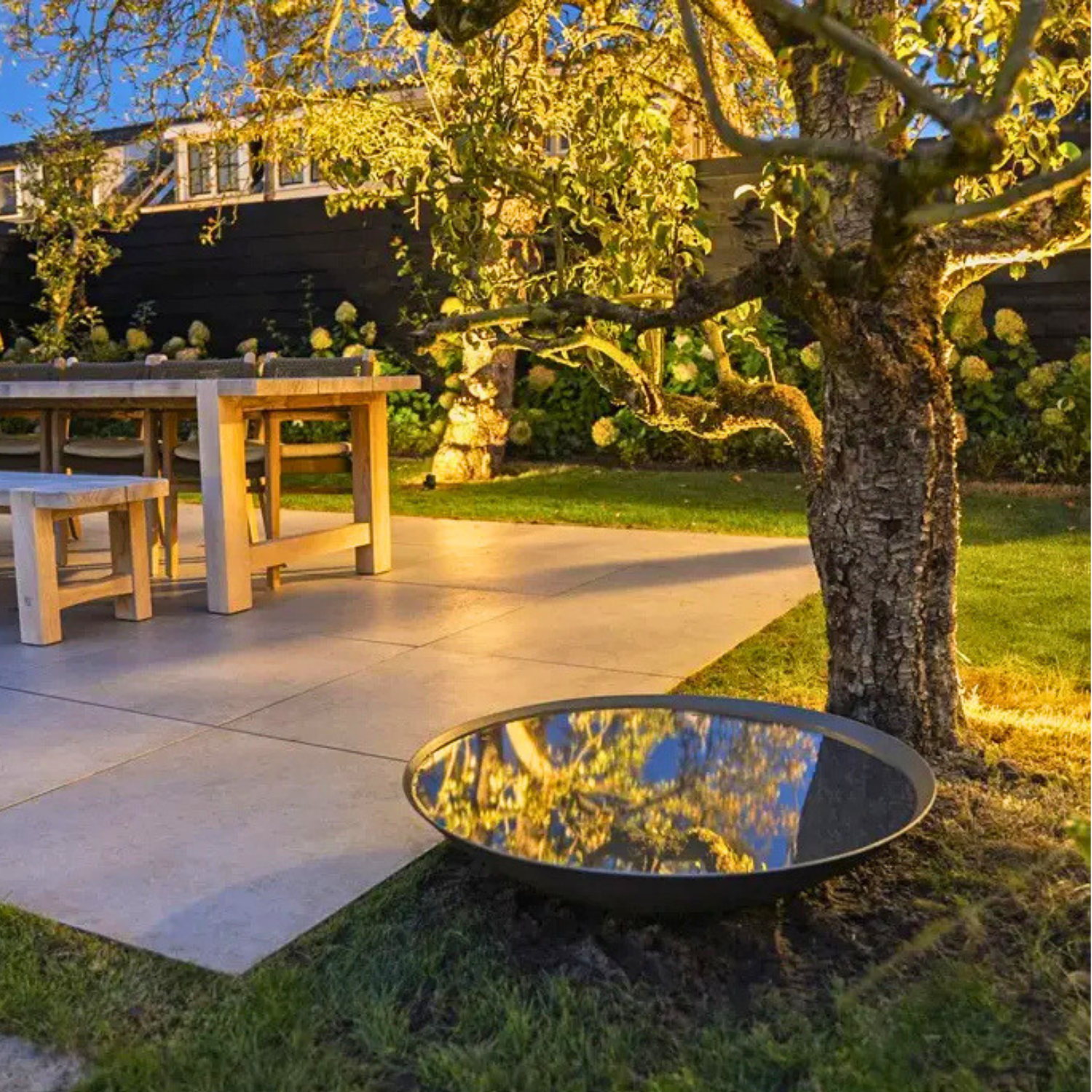 Modern powder coated steel water bowl creating reflective still water in a landscaped gravel garden.