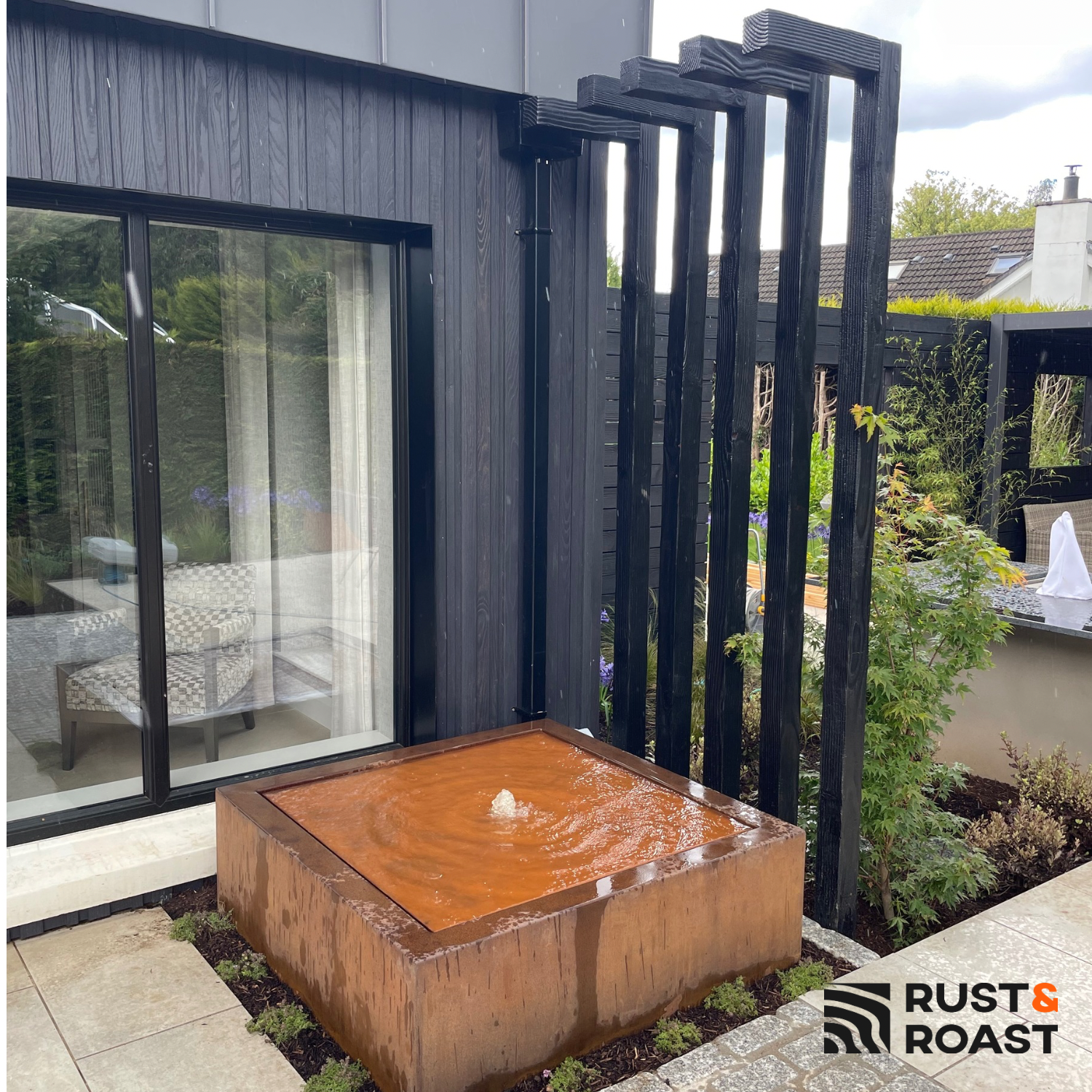 Square corten steel water feature beside a modern house