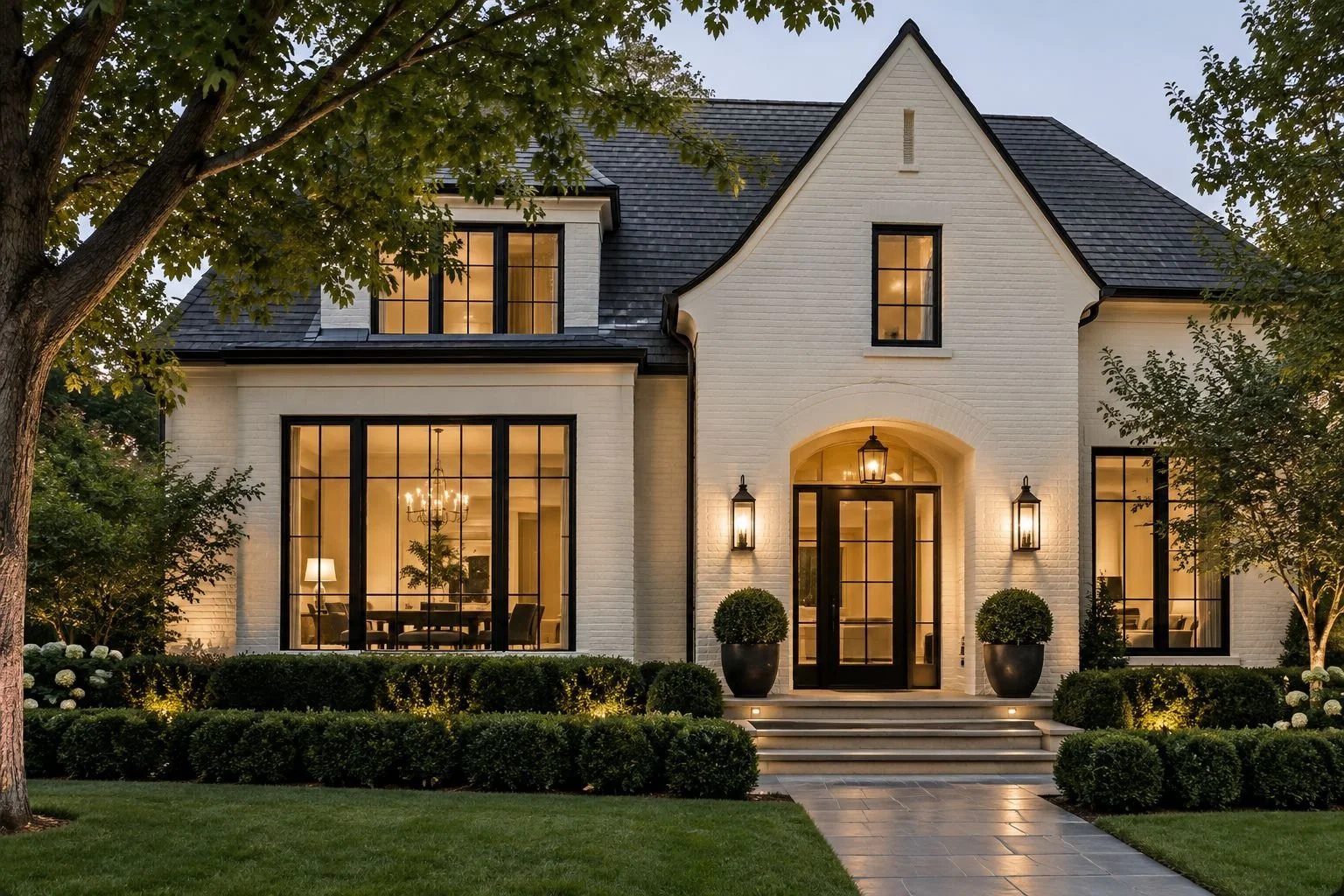 Cream painted brick home with black windows and lantern lights at dusk